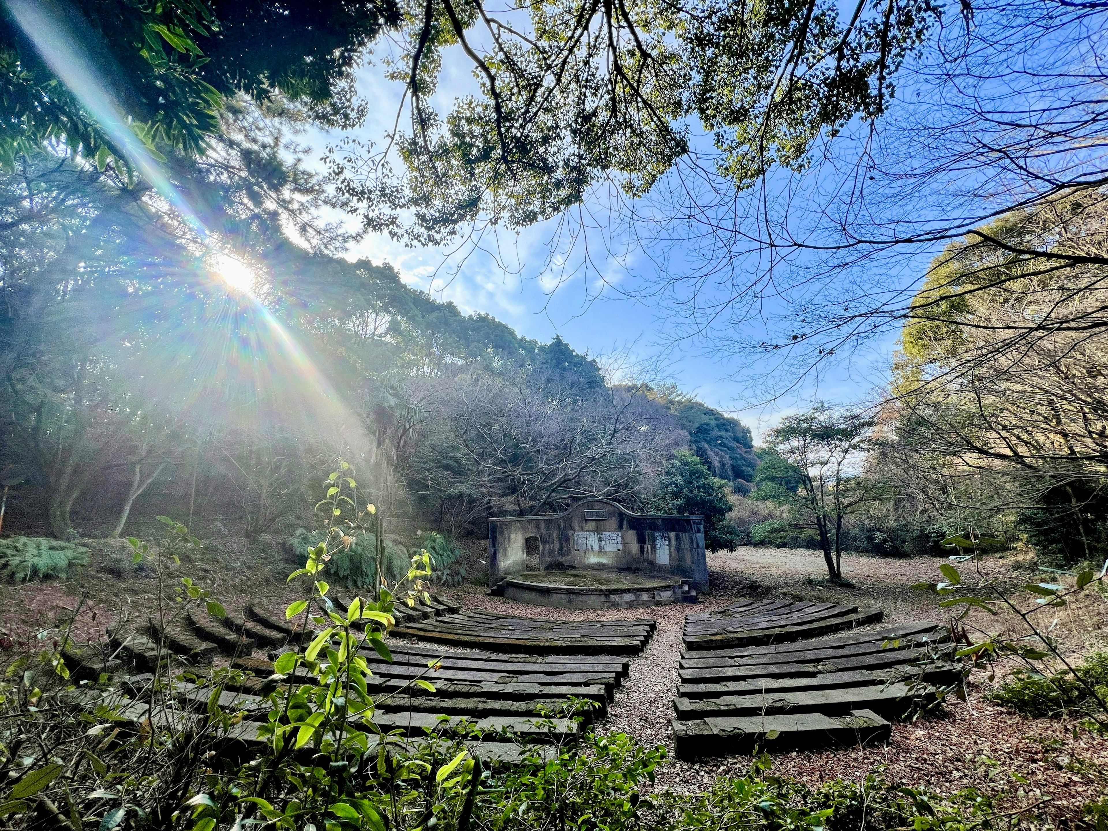 An outdoor amphitheater surrounded by trees with a vintage building