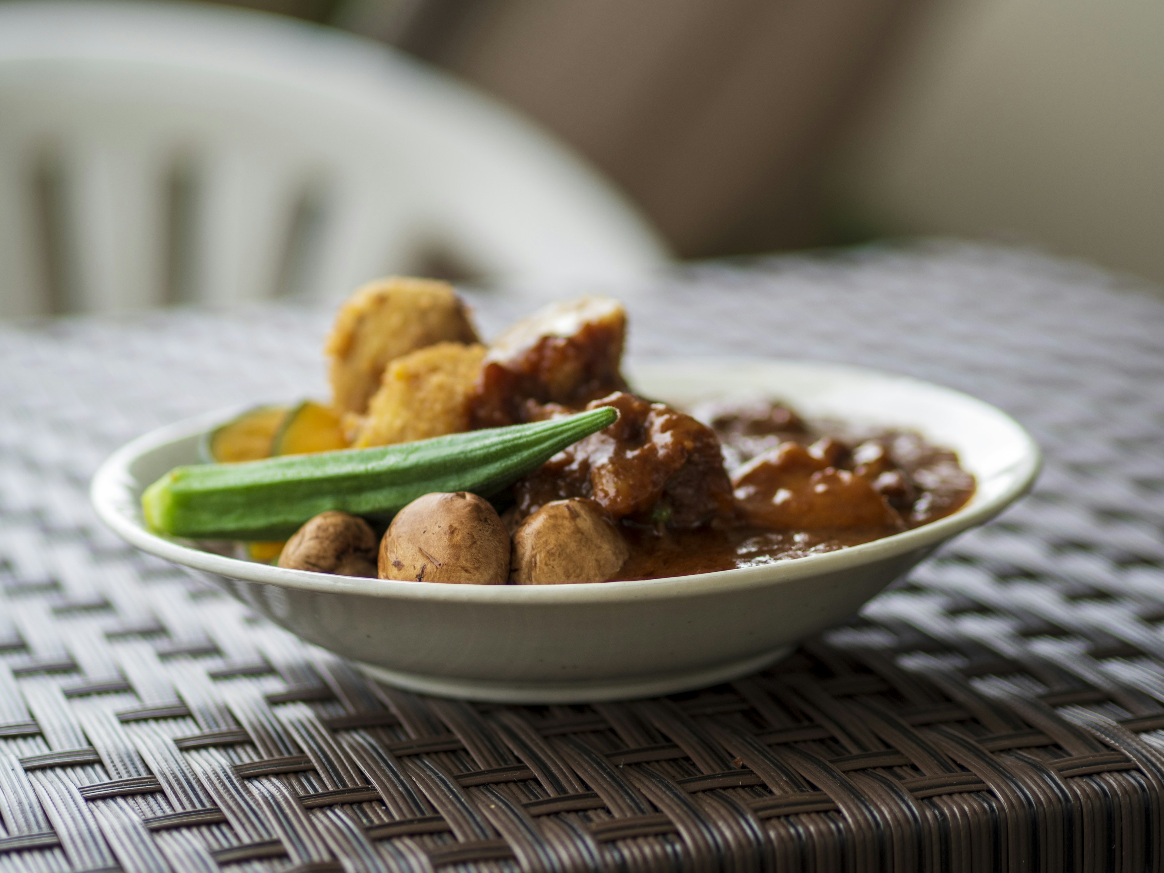 Un tazón de curry con albóndigas servido con okra verde y frituras en una mesa texturizada