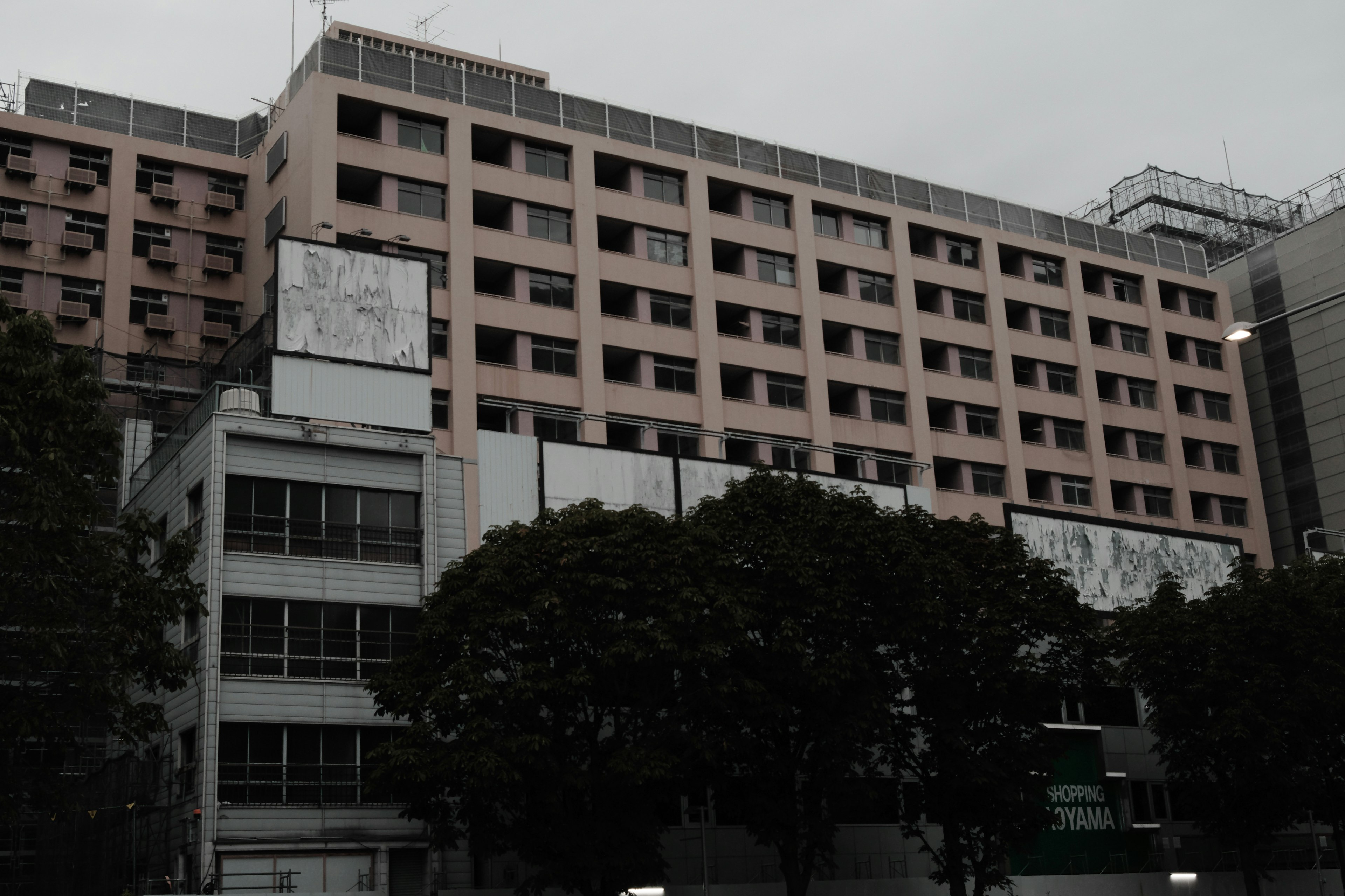 Exterior view of a building under gray clouds featuring pink walls and green trees