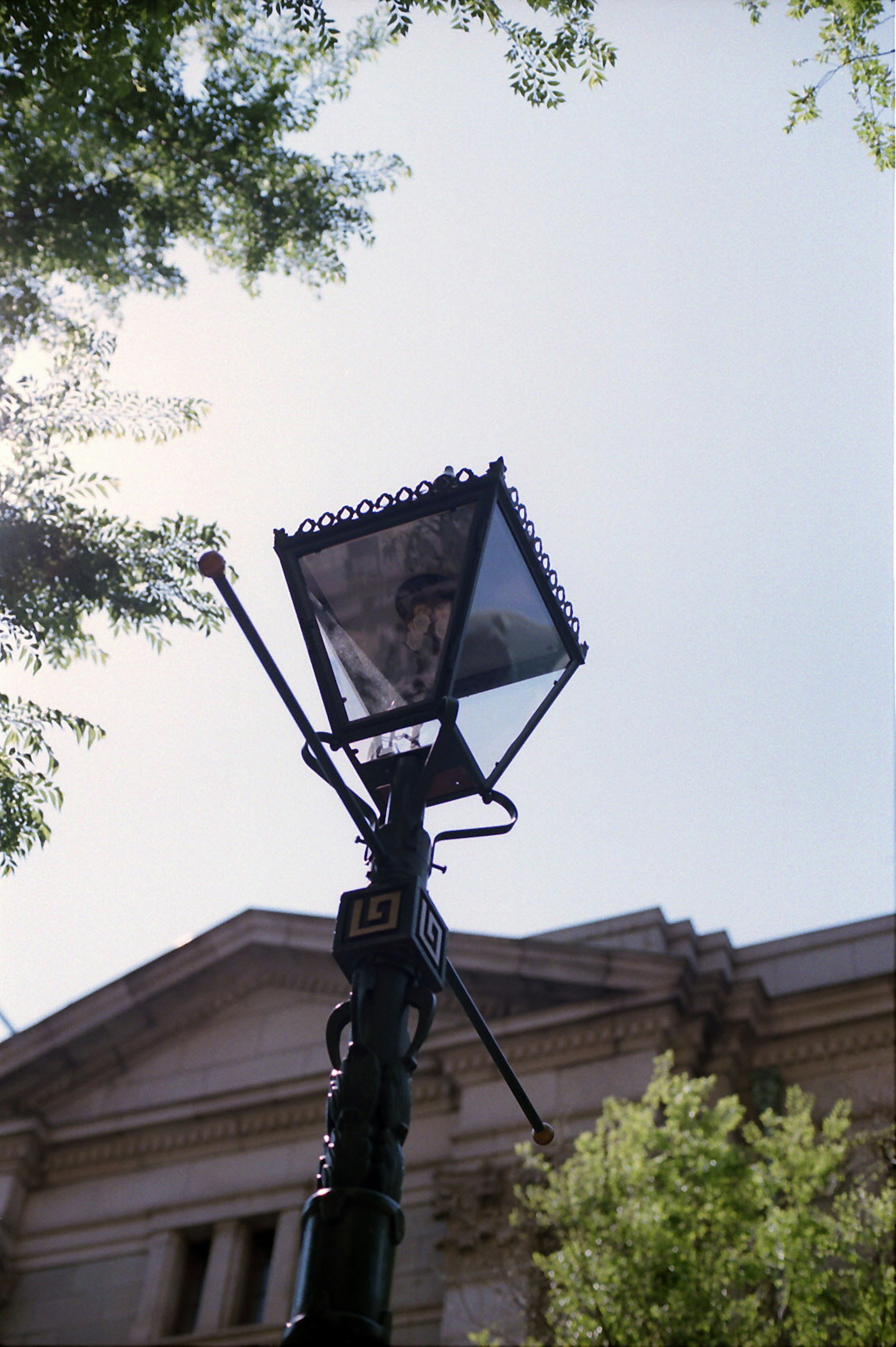 Low-angle view of a street lamp with green trees and bright sky in the background