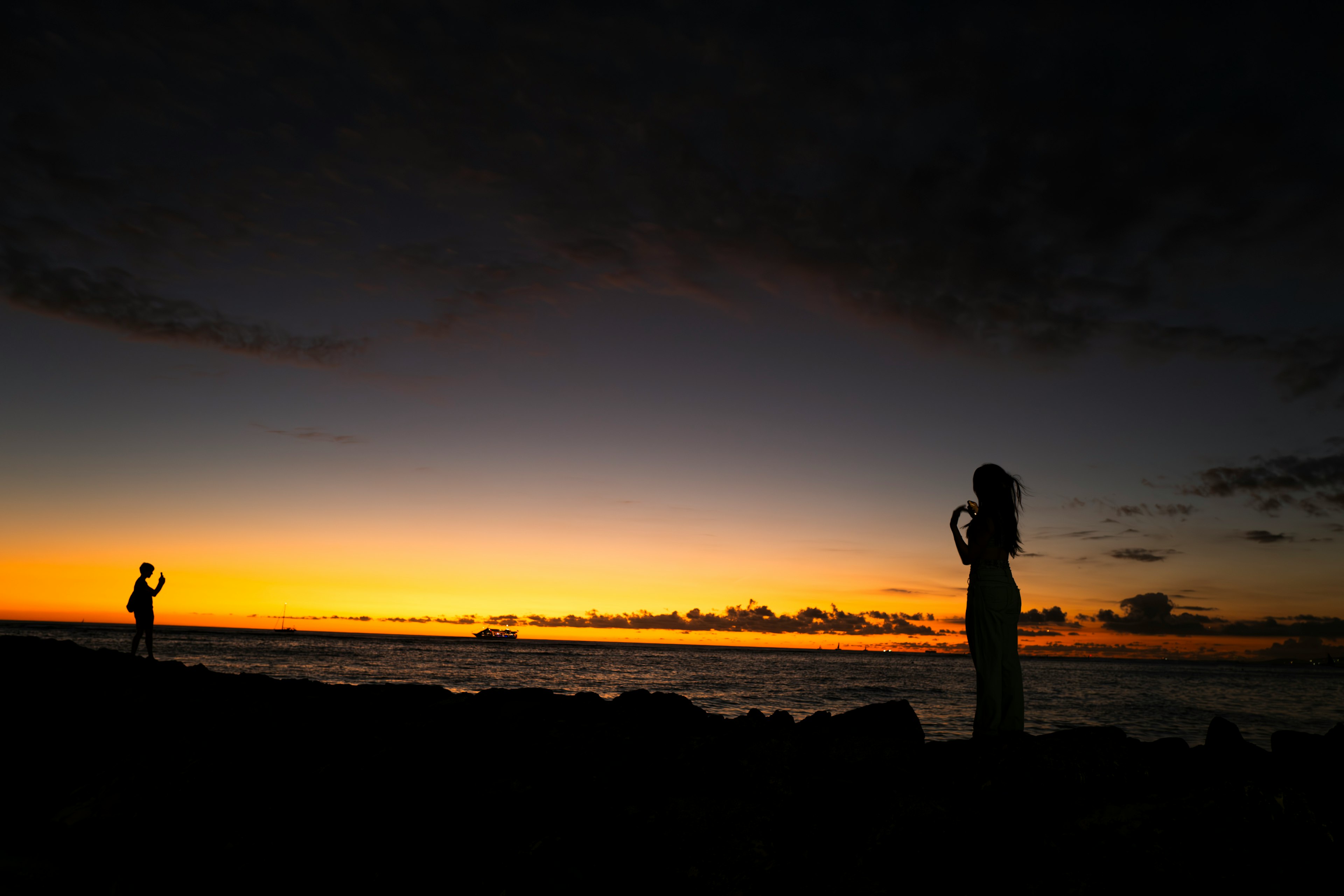 夕焼けの海辺でシルエットの人物が立つ風景