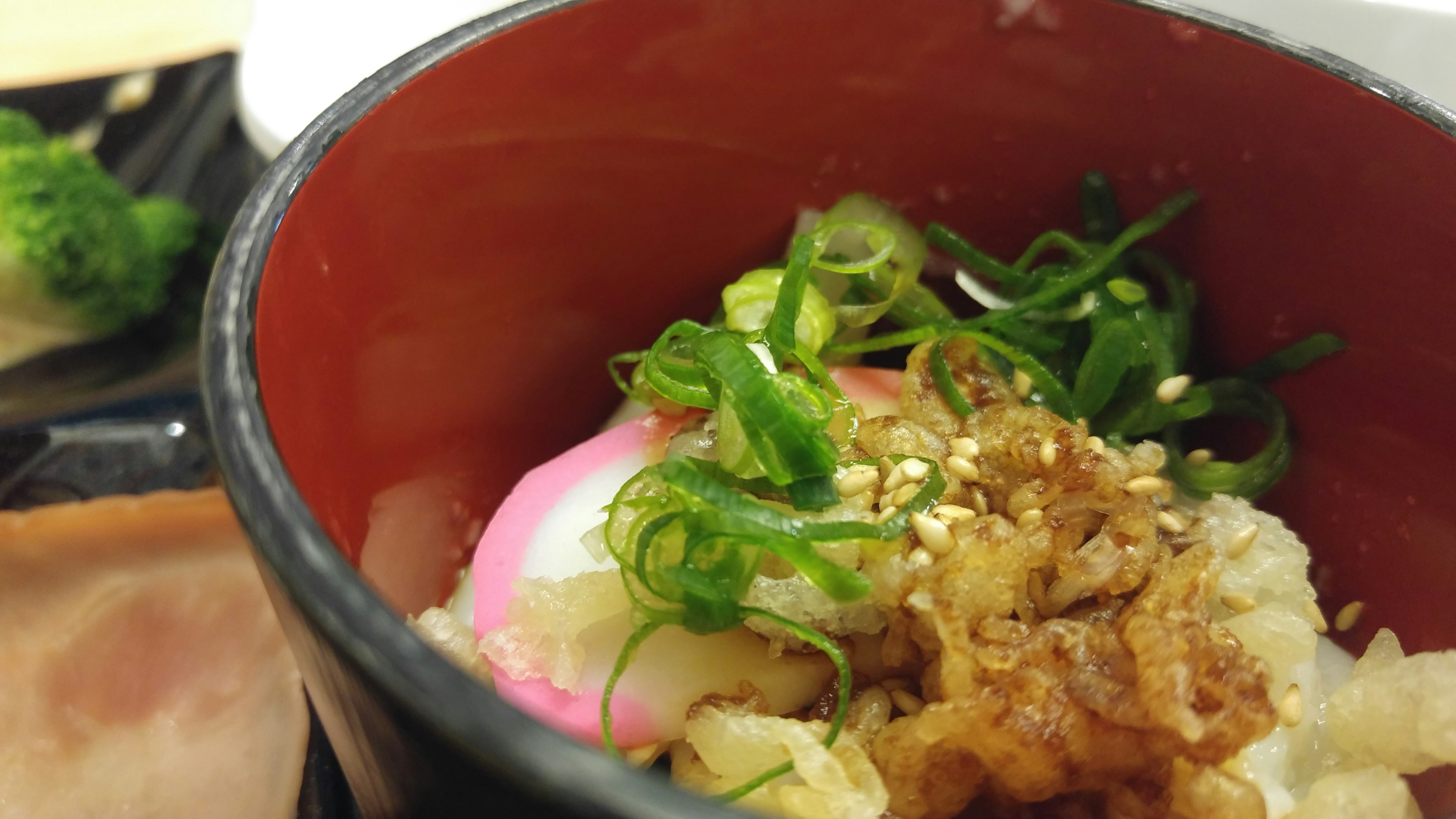 Rice in a red bowl topped with green onions and garnishes