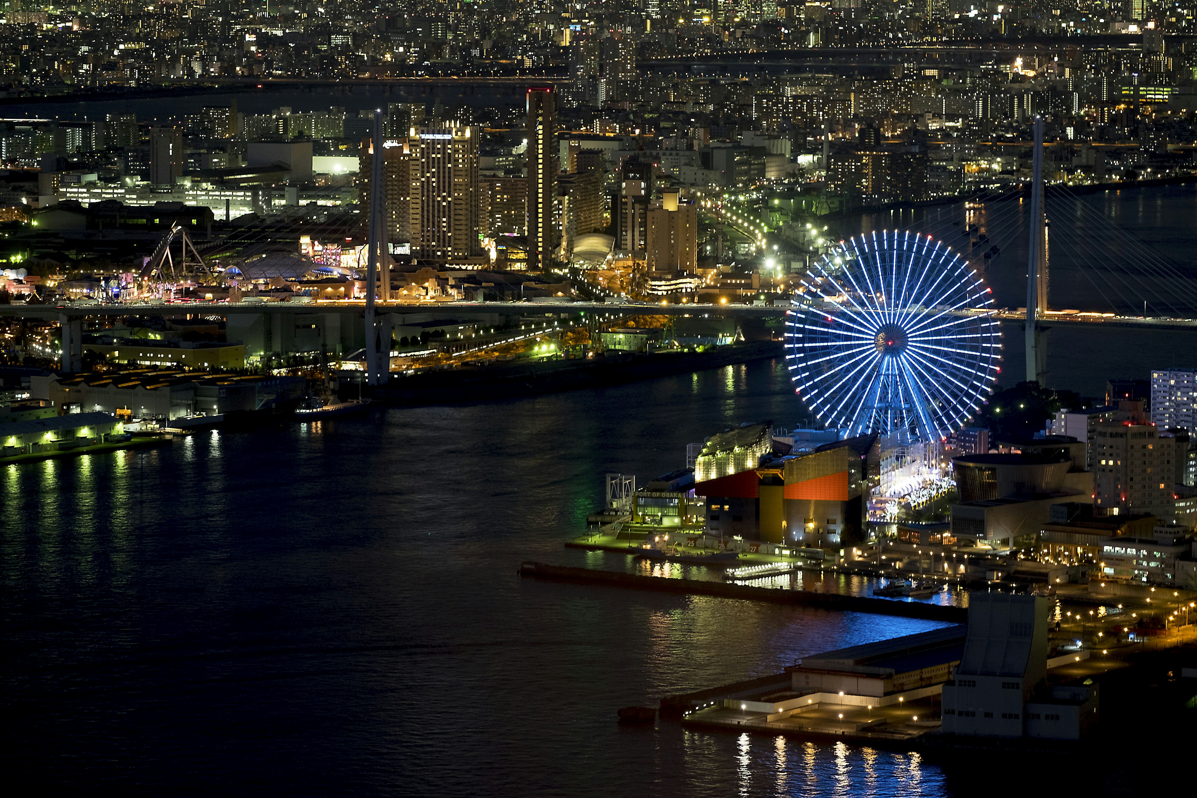 Stadtansicht bei Nacht mit einem beleuchteten Riesenrad und Hafen