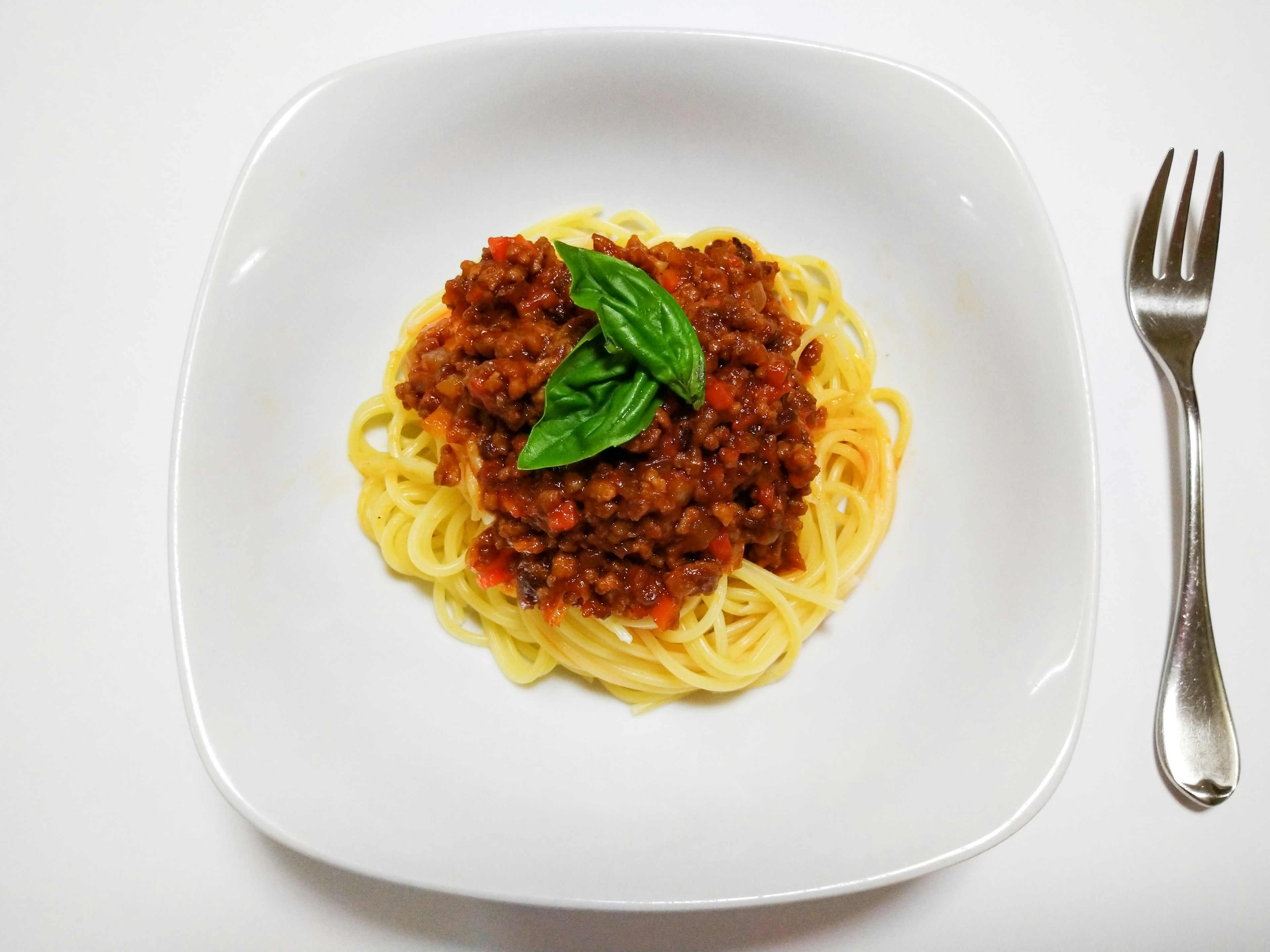 Spaghetti à la sauce viande garni de basilic frais dans une assiette blanche