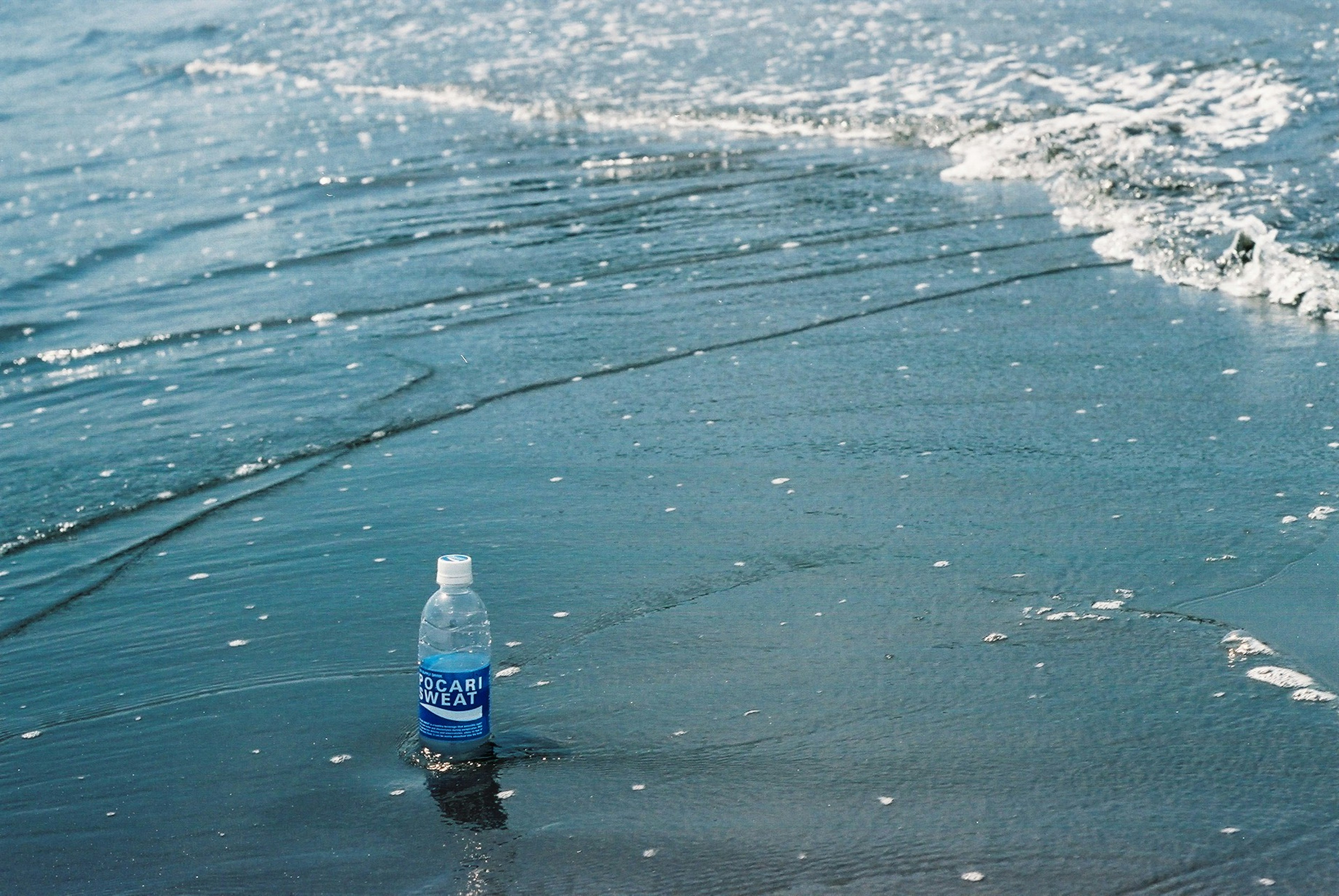 Botol air di pantai dengan ombak yang membasahi pasir