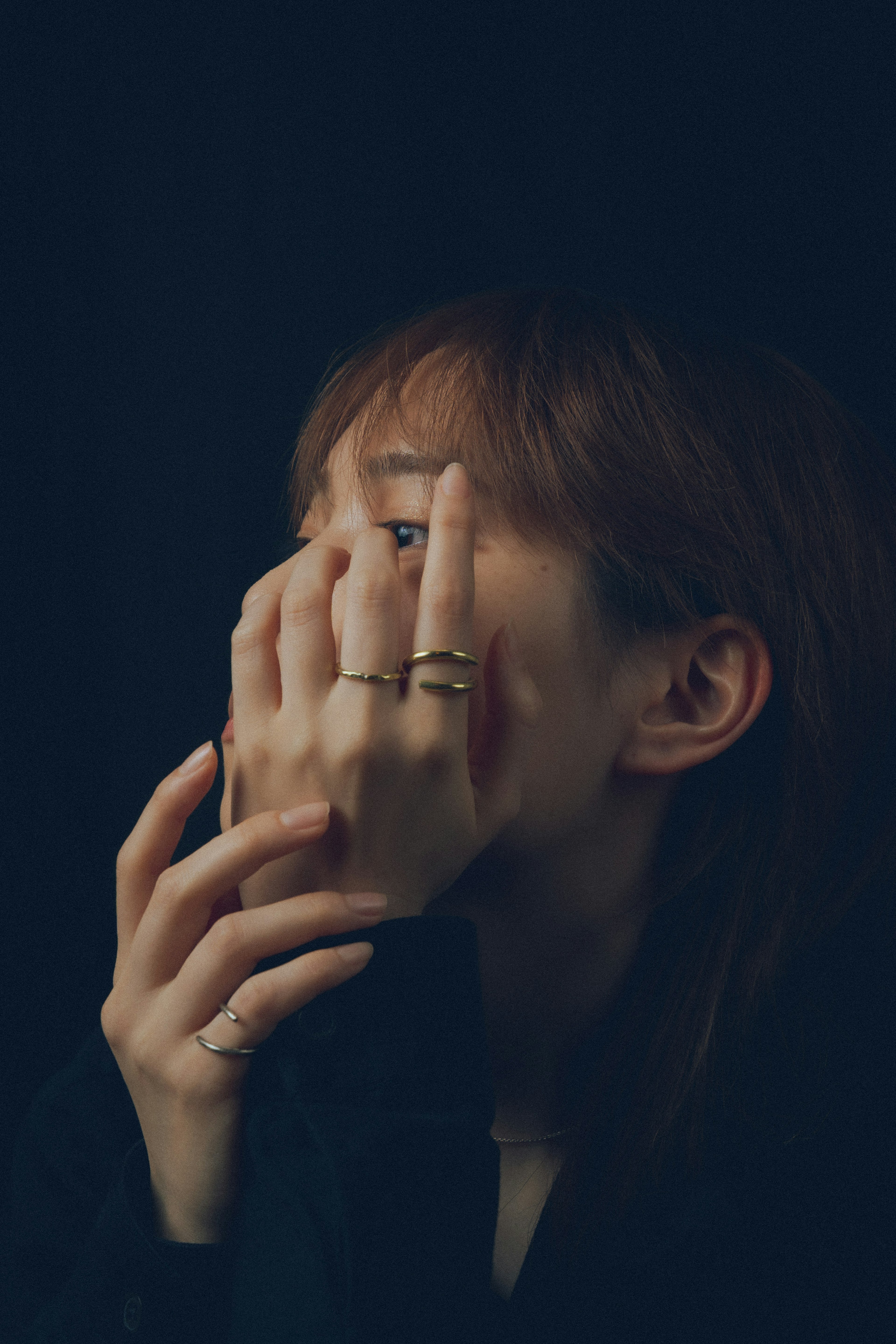 Portrait of a woman hiding her face with her hands against a dark background