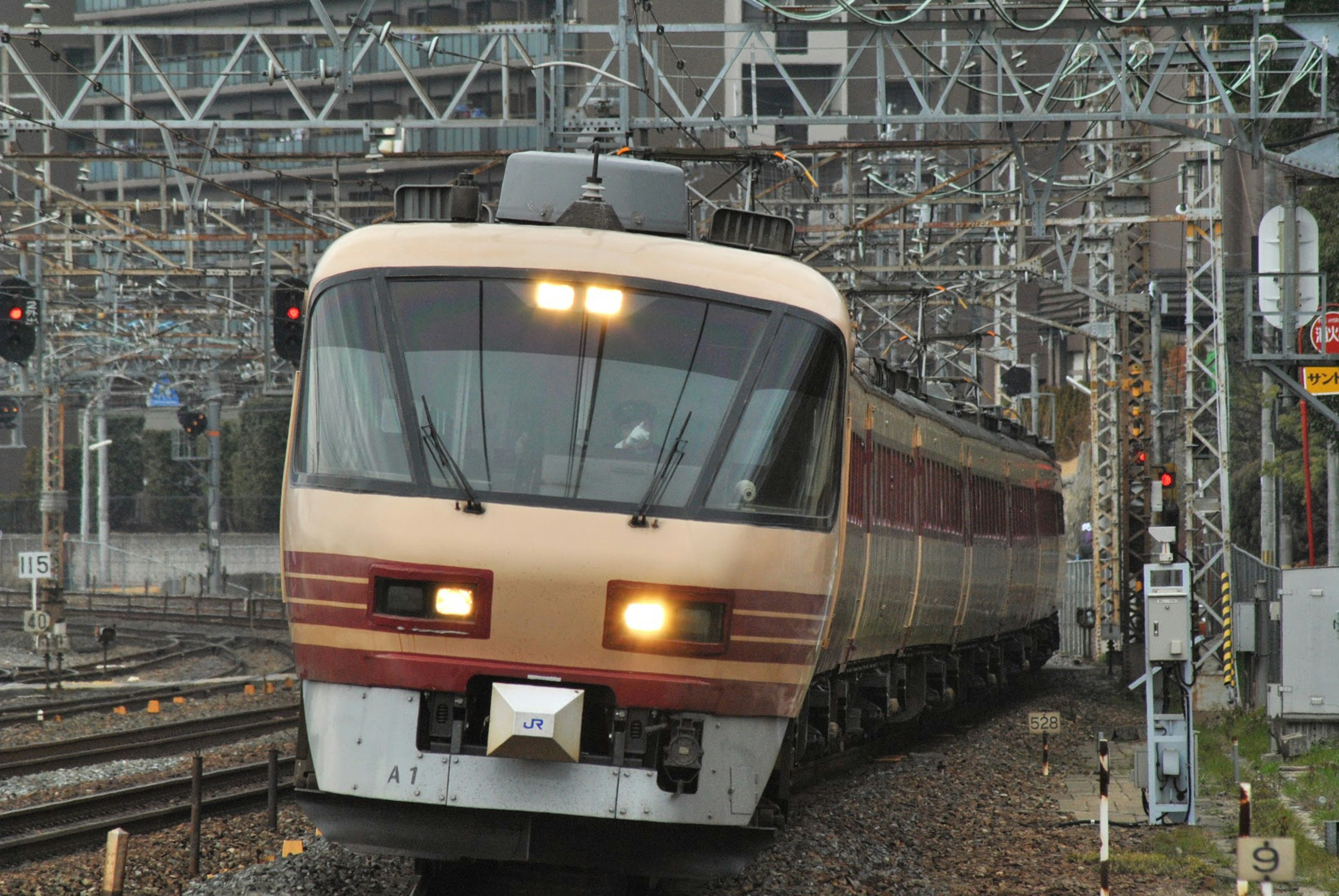 A brown train navigating railway tracks surrounded by signals and overhead lines