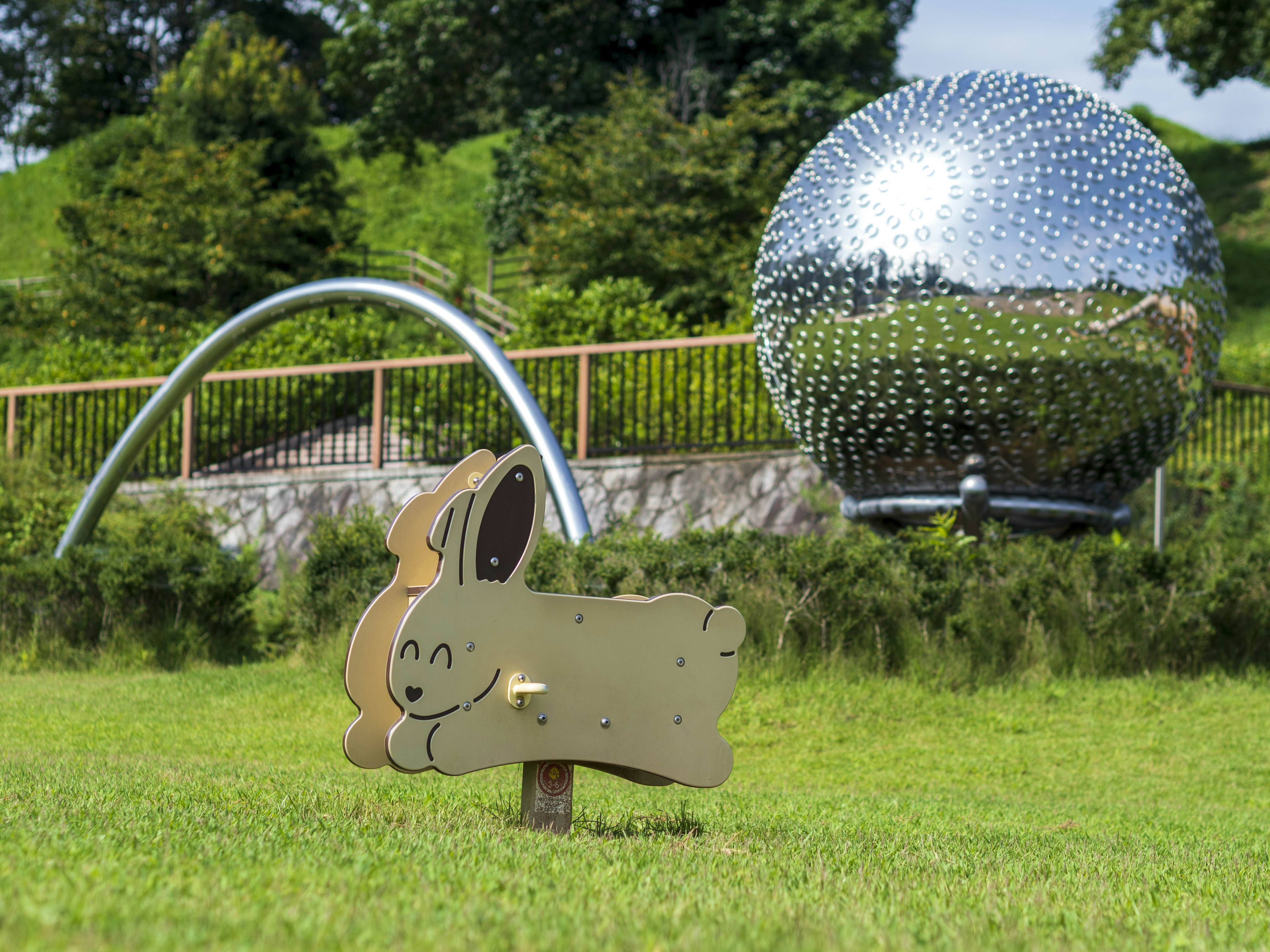 A wooden rabbit sculpture on green grass with a reflective spherical sculpture in the background