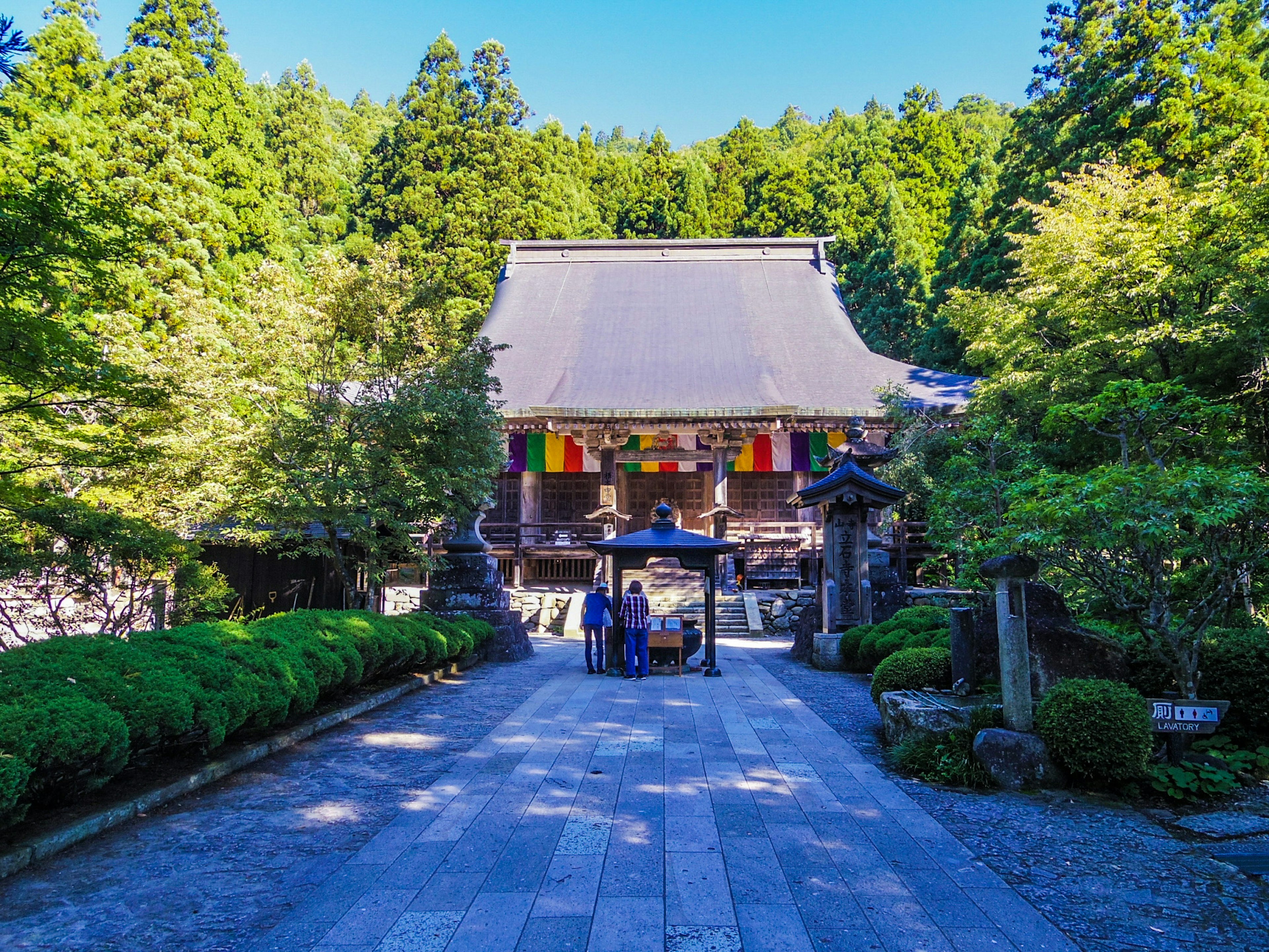 Traditional Japanese temple surrounded by lush greenery vibrant flags displayed on the roof serene stone pathway