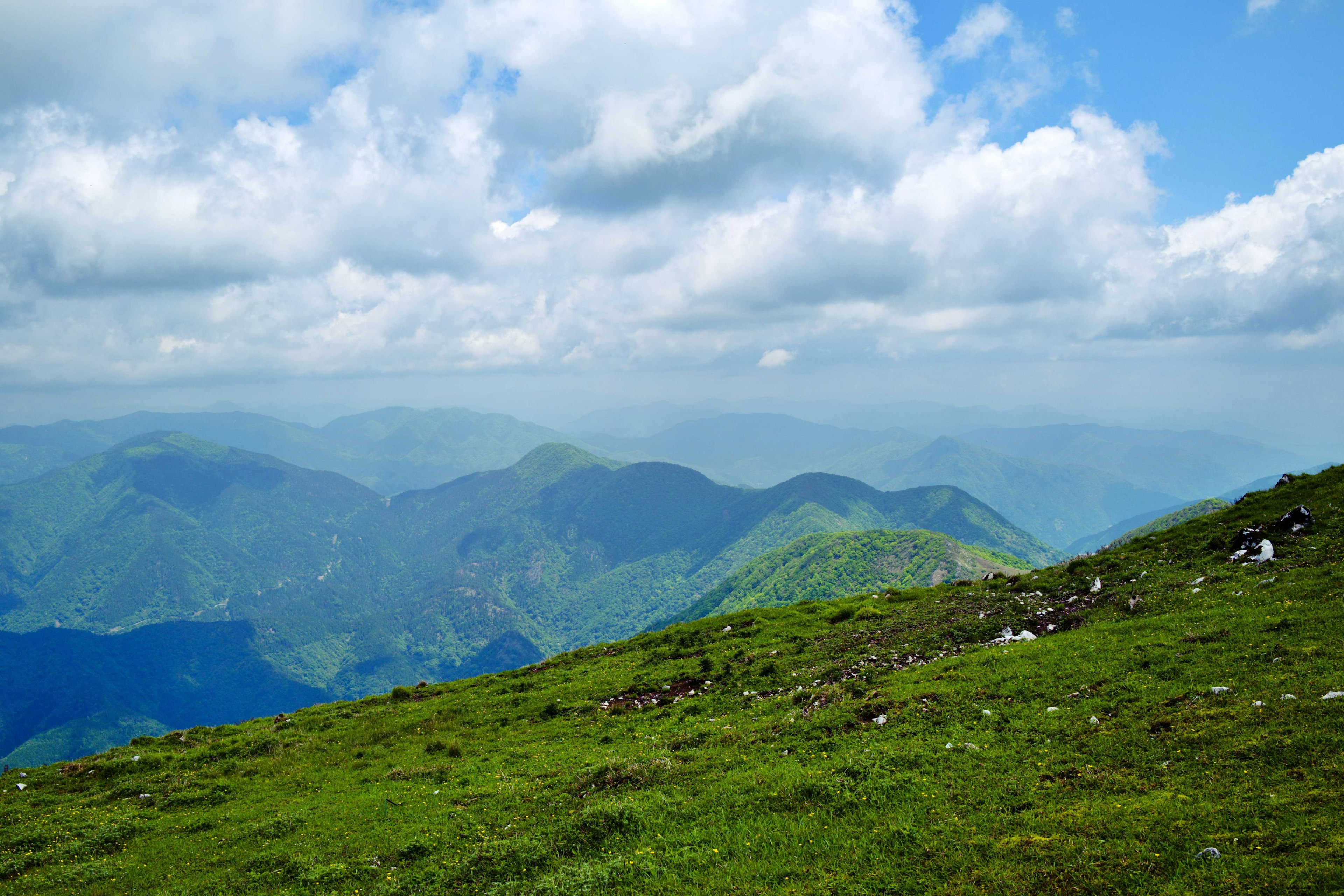 Mountain landscape featuring green grass and blue sky with white clouds