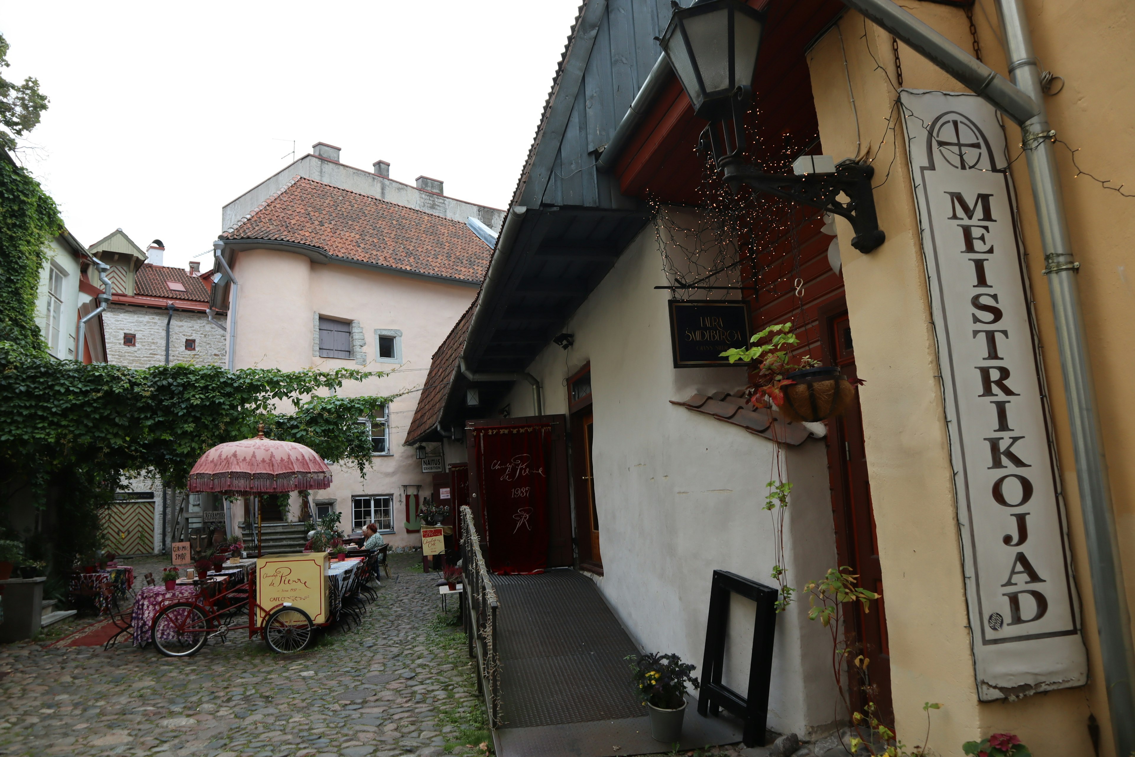 Charmante Kopfsteinpflastergasse mit dem Schild Meistrikojad und einem Caféschirm