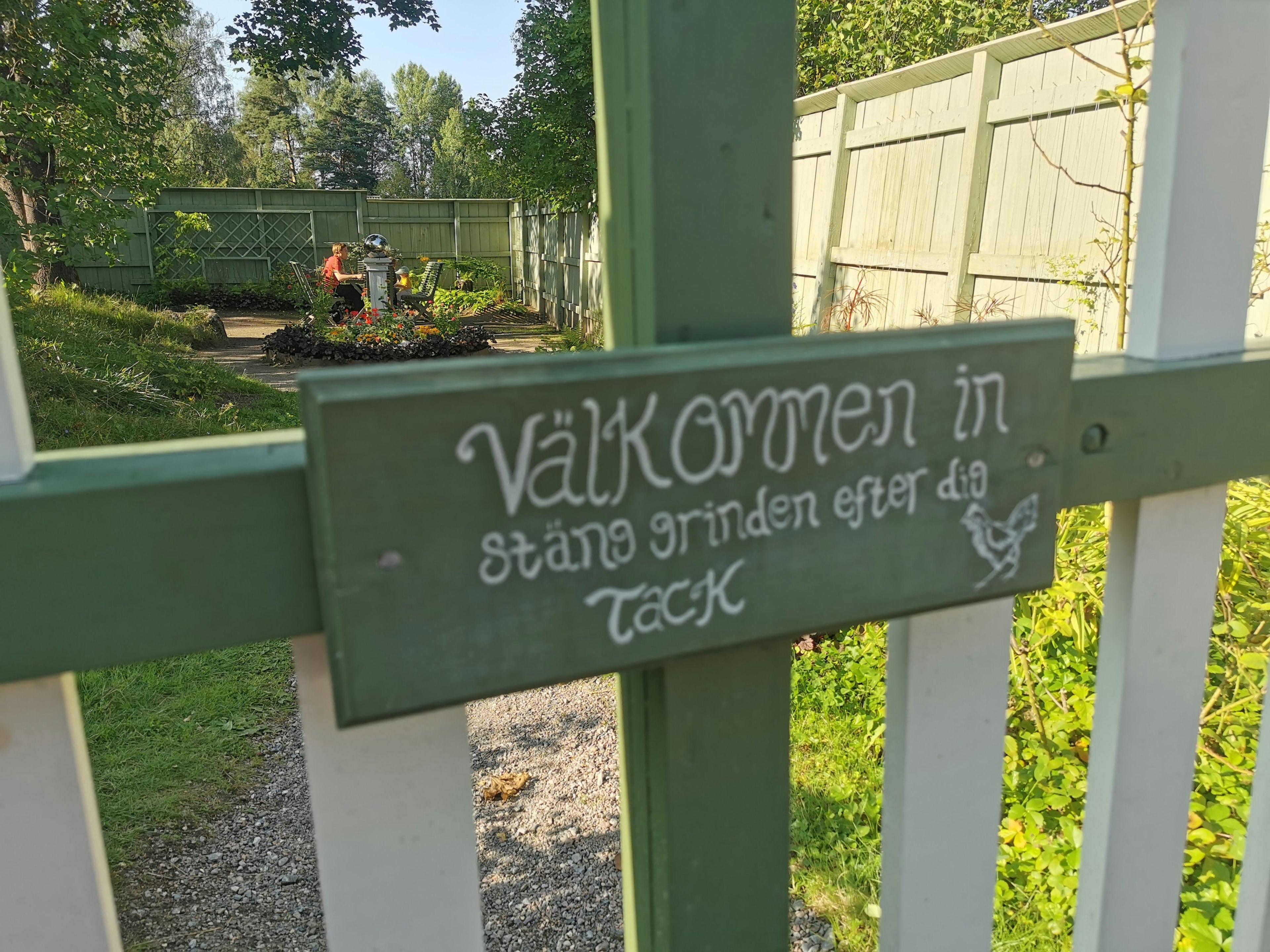 Entrée d'un jardin avec un panneau de bienvenue sur une clôture verte