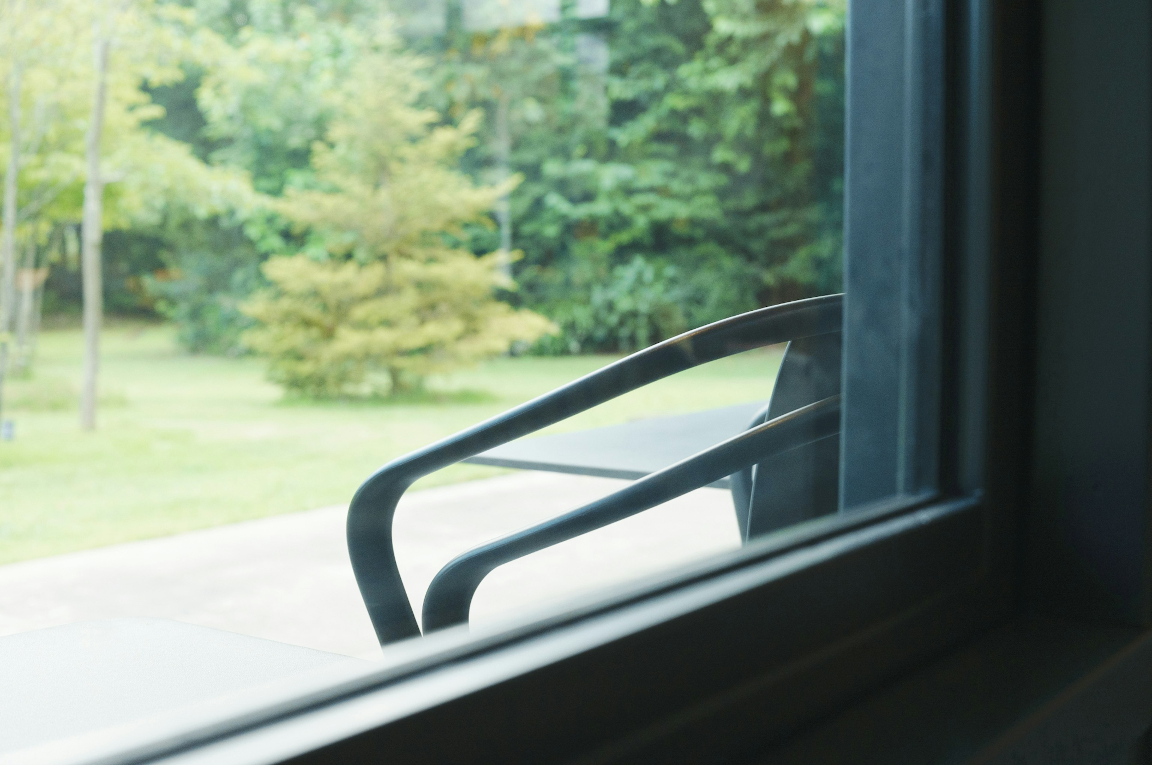 Blick auf einen grünen Garten und einen Teil eines schwarzen Stuhls von einem Fenster aus