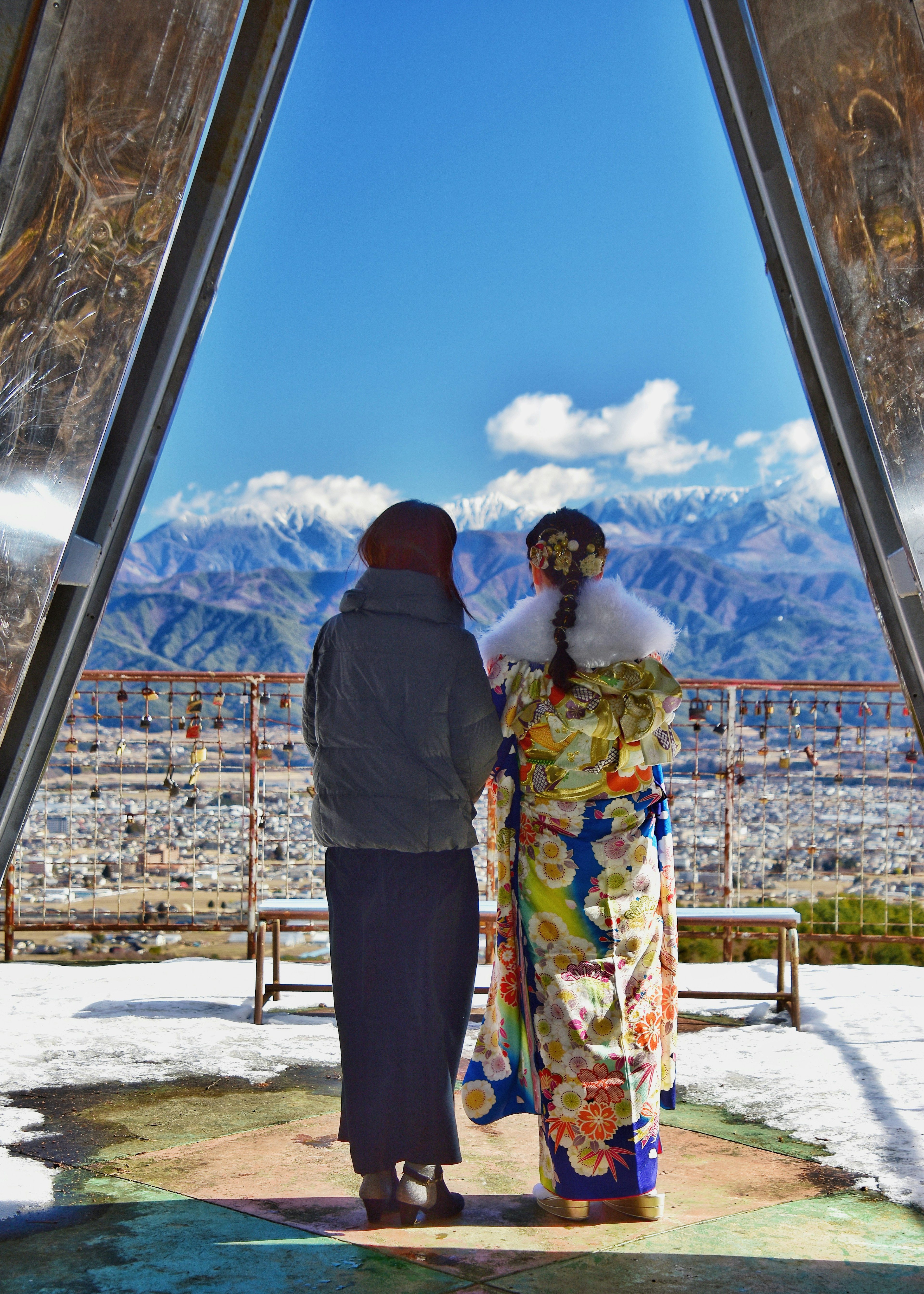 Un homme en tenue décontractée et une femme en kimono coloré se tenant dans un paysage enneigé avec des montagnes en arrière-plan