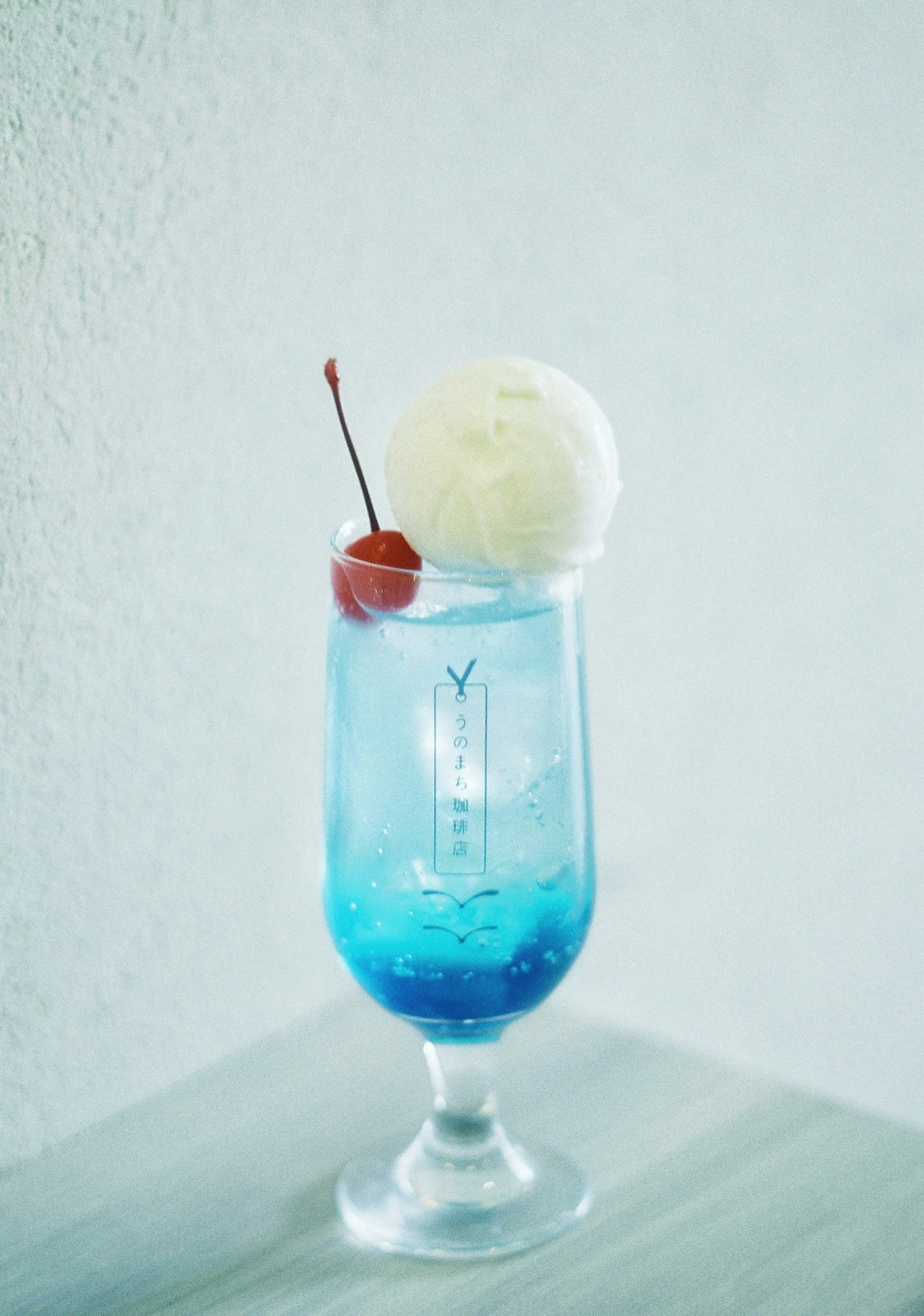 Ein blauer Drink mit weißem Eis und einer Kirsche in einem hohen Glas