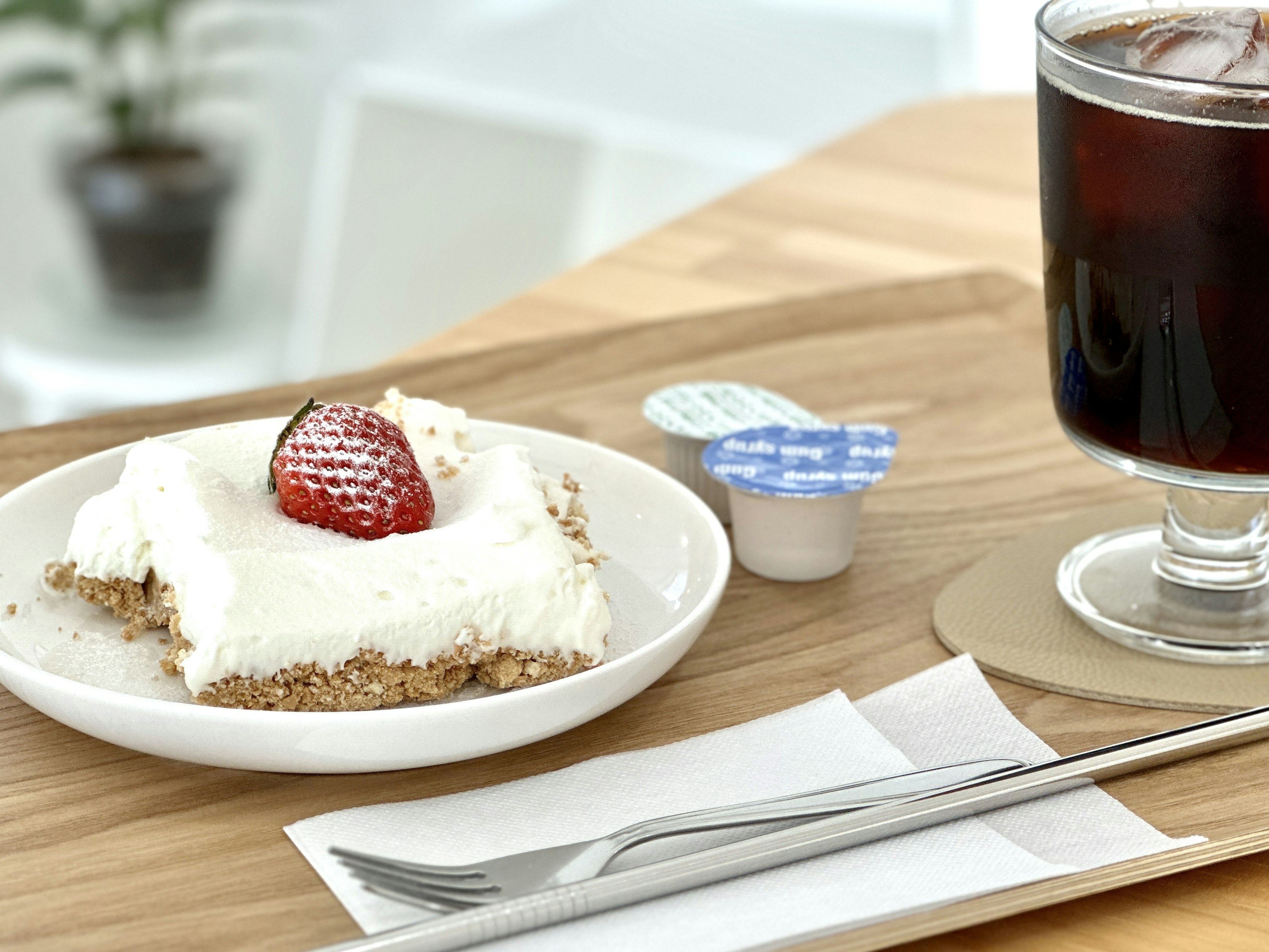 Dessert with cream and a strawberry topping alongside a cup of coffee on a wooden table