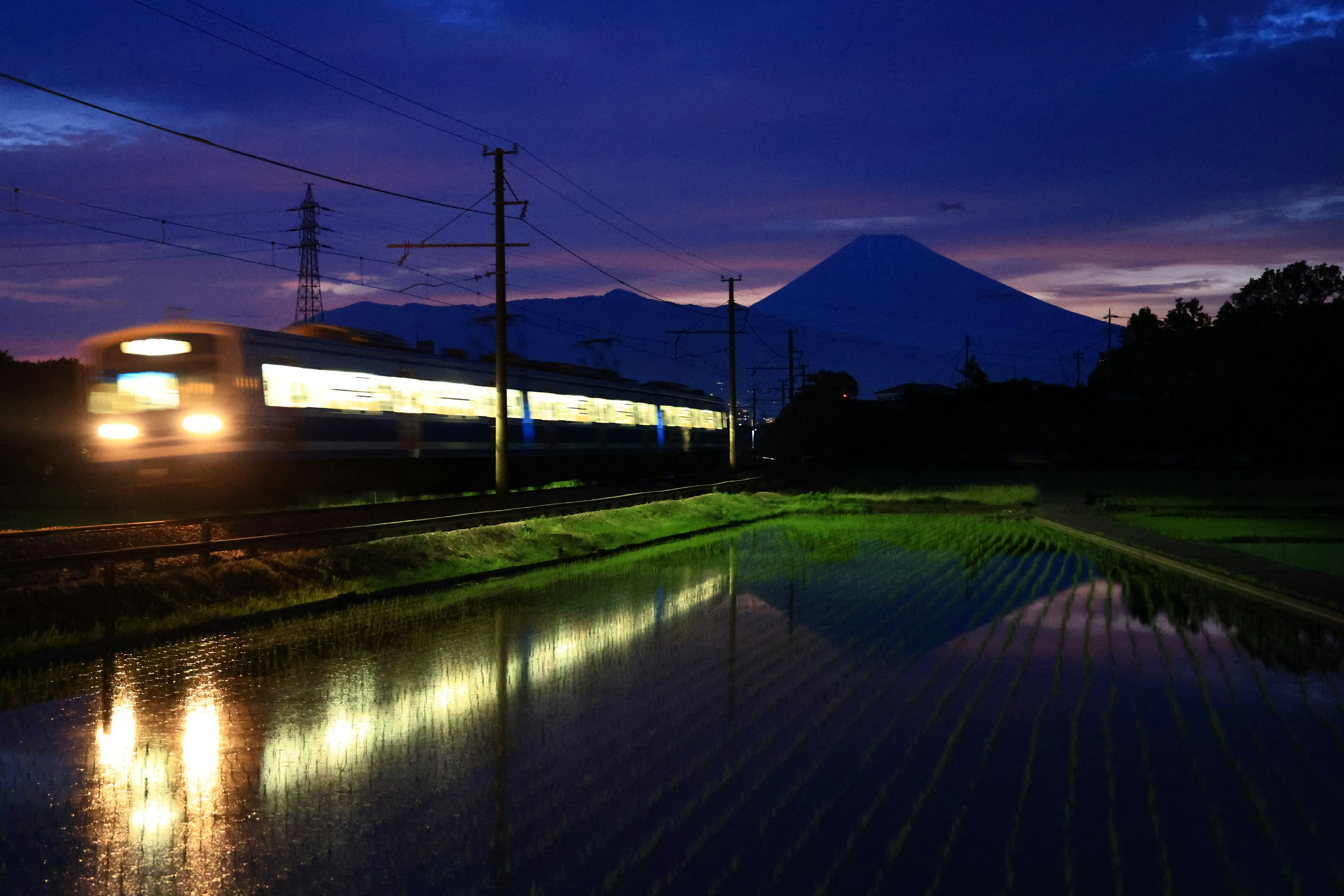 Scenic view of Mount Fuji with a train at dusk reflecting in rice fields