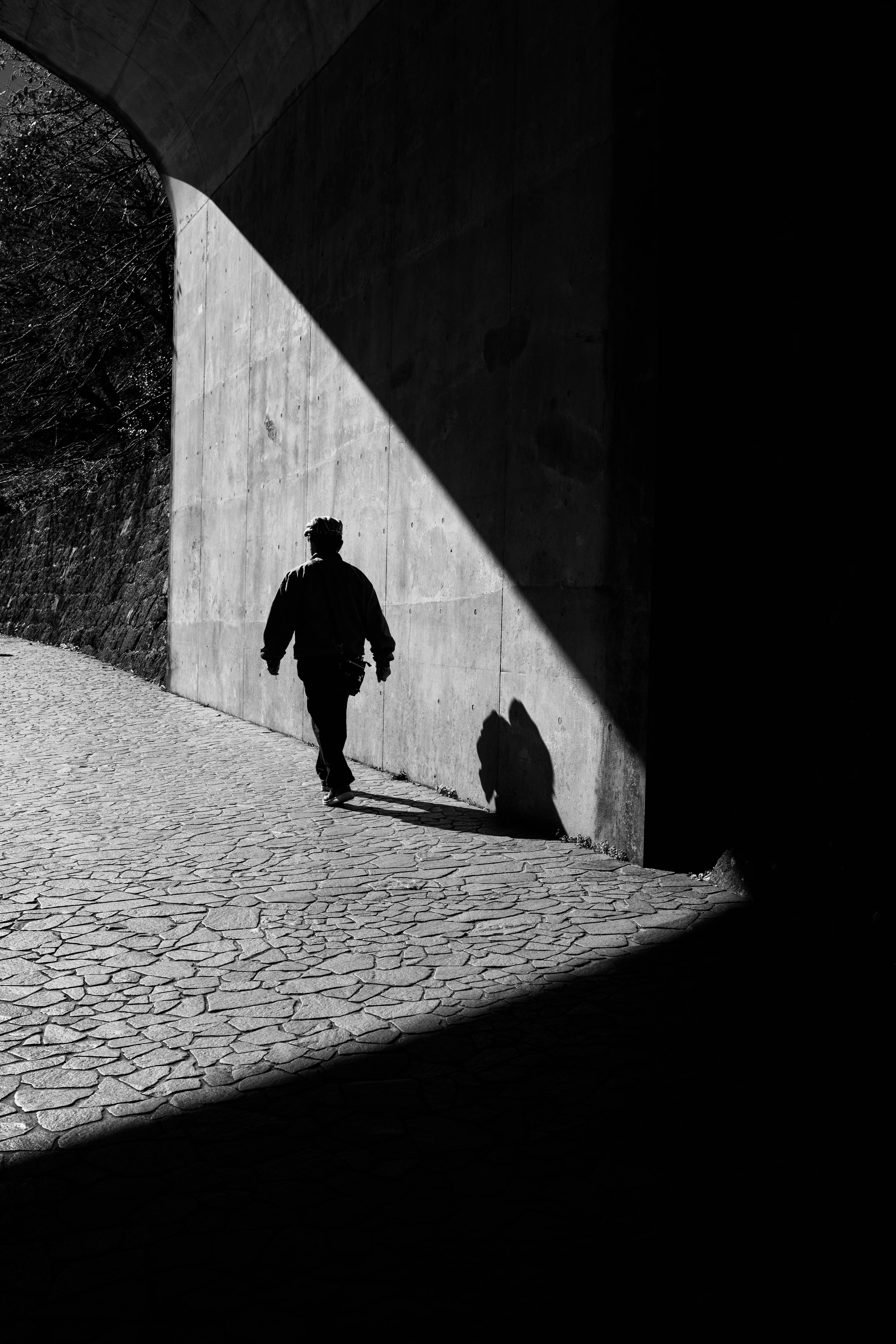 A monochrome photo highlighting the contrast of shadow and light with a person walking