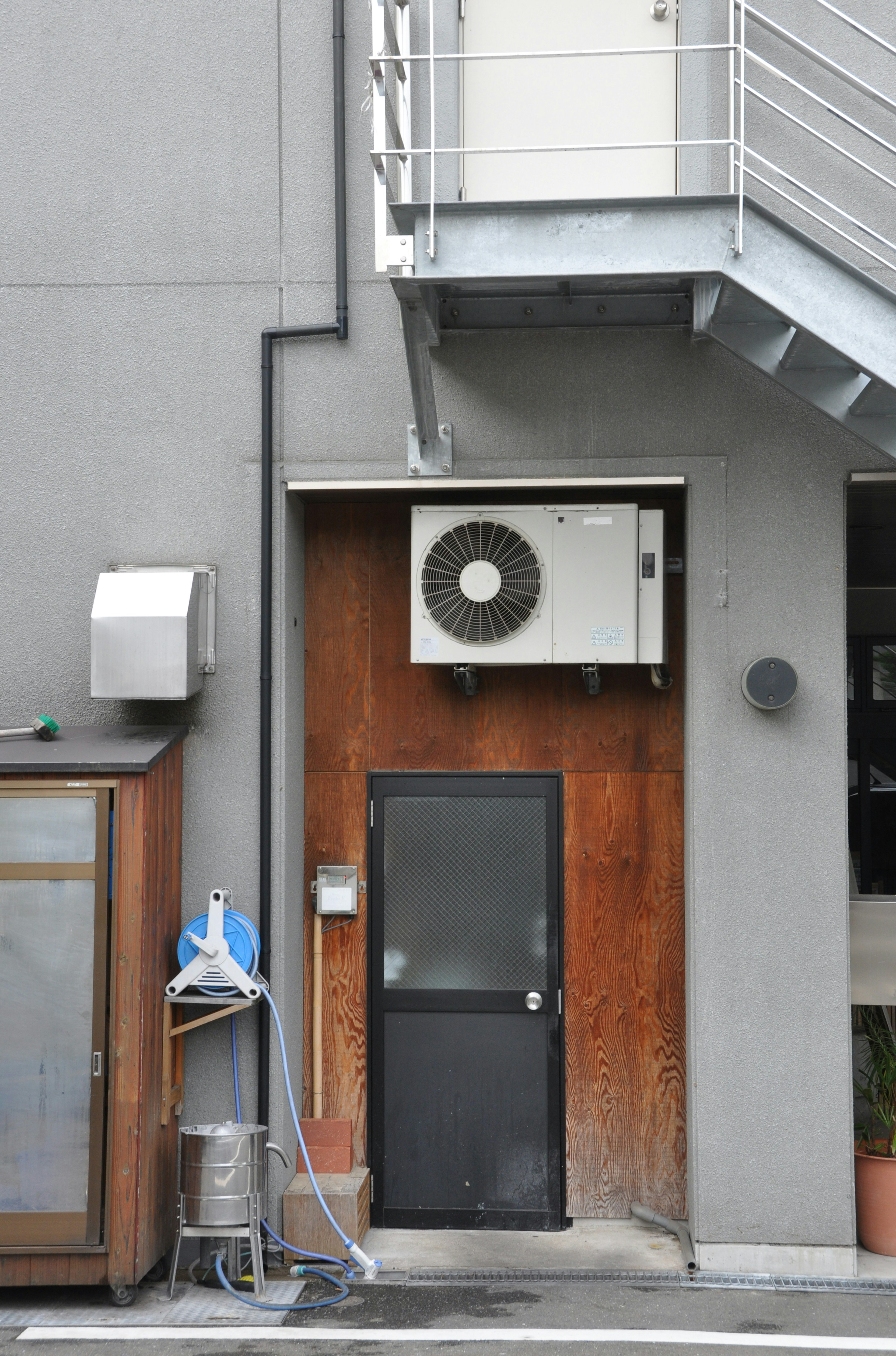 Extérieur d'un bâtiment gris avec une porte en bois et une unité de climatisation