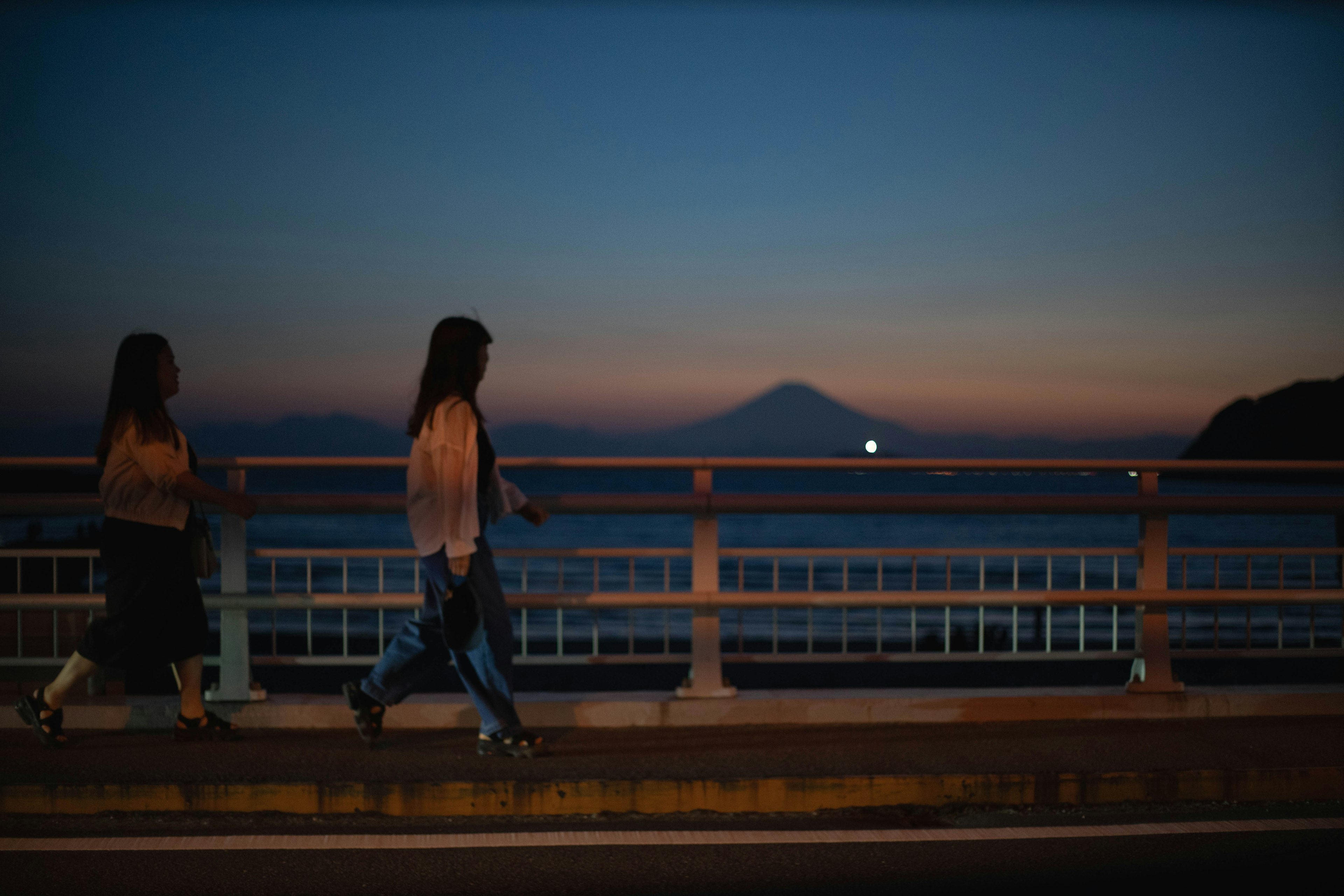 Dos mujeres caminando por un puente al anochecer con el monte Fuji de fondo