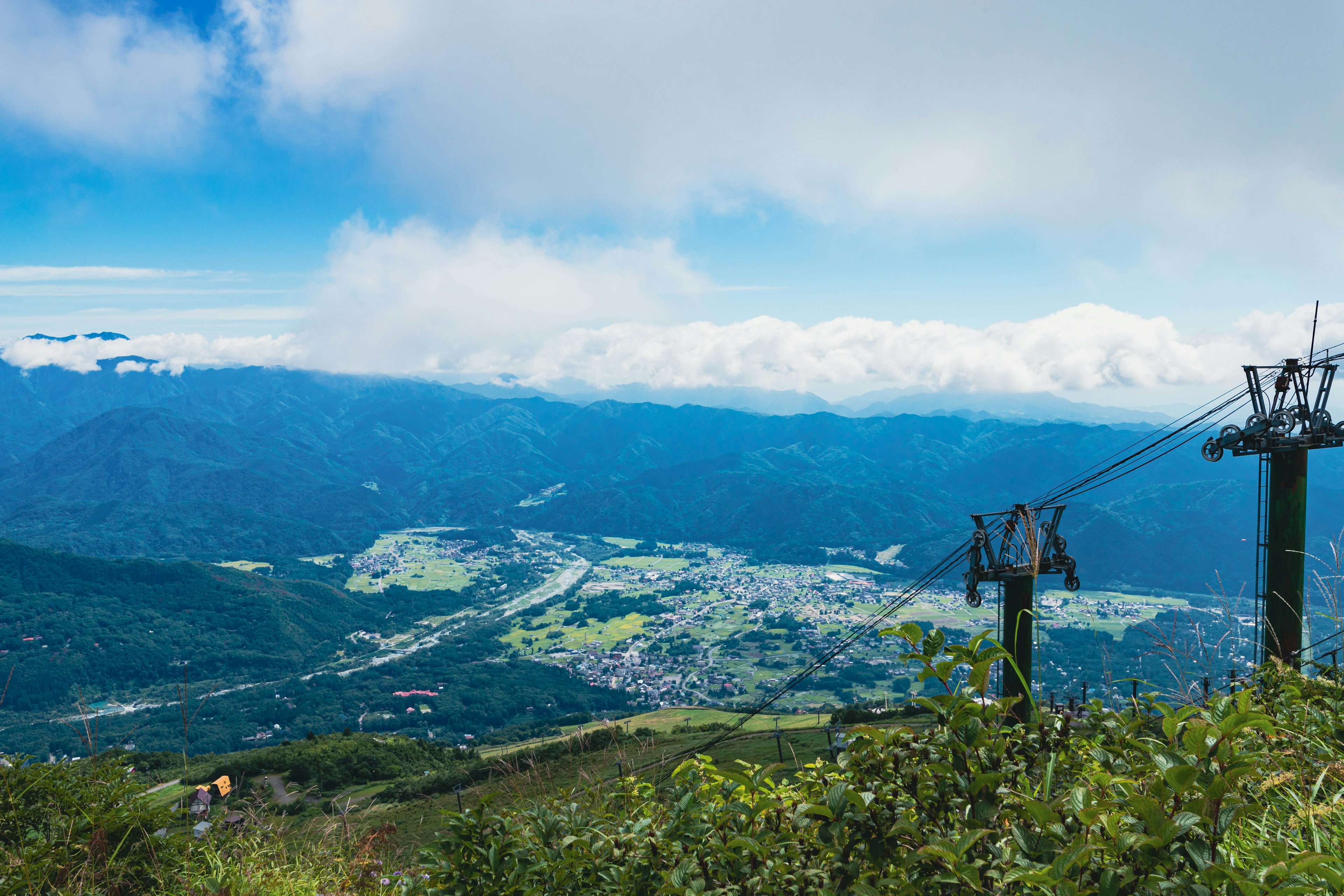 Vista escénica desde la cima de una montaña que muestra cielos azules y nubes sobre un valle verde y una ciudad