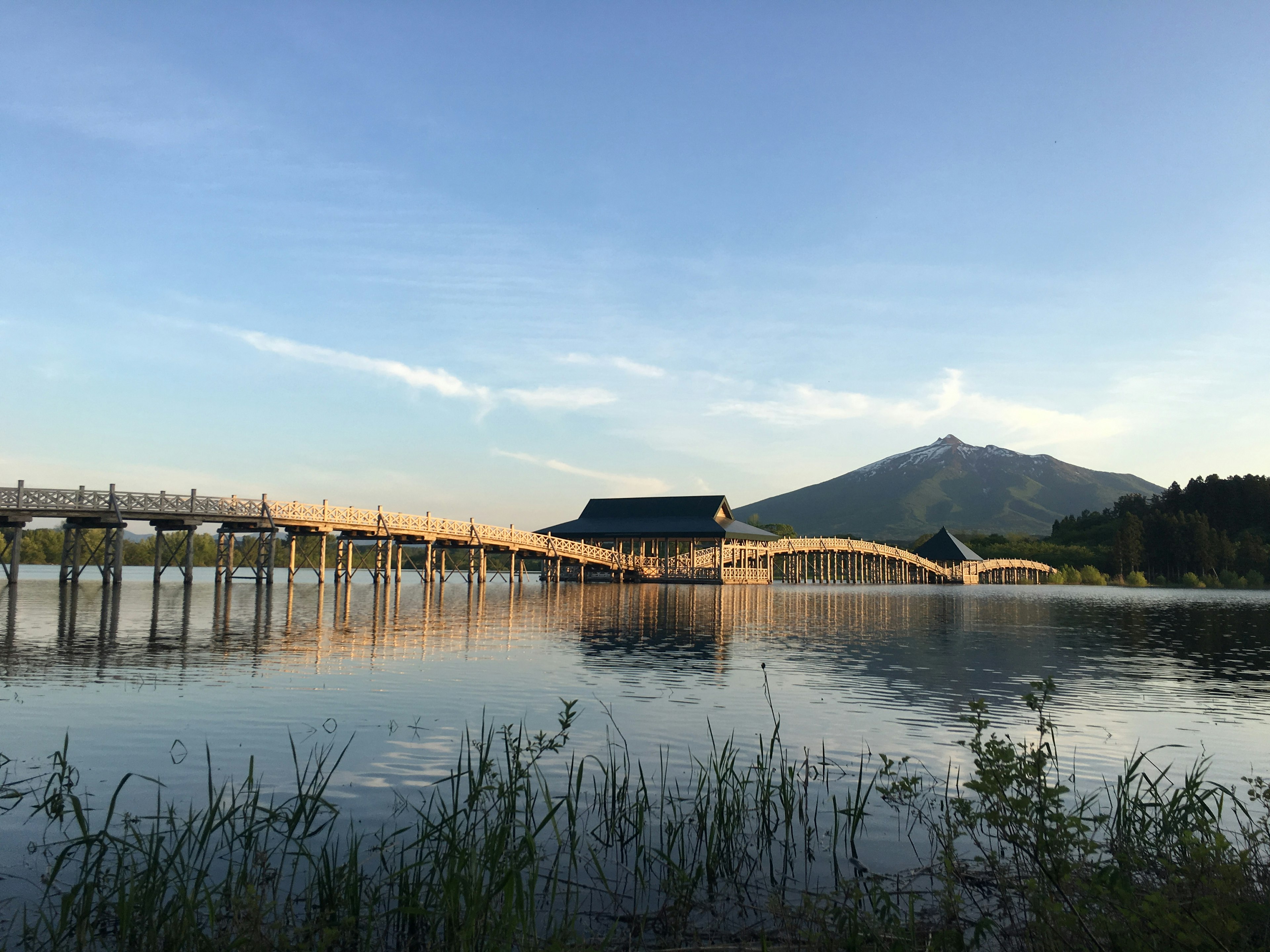 Pemandangan jembatan kayu yang memantul di air dengan gunung di latar belakang