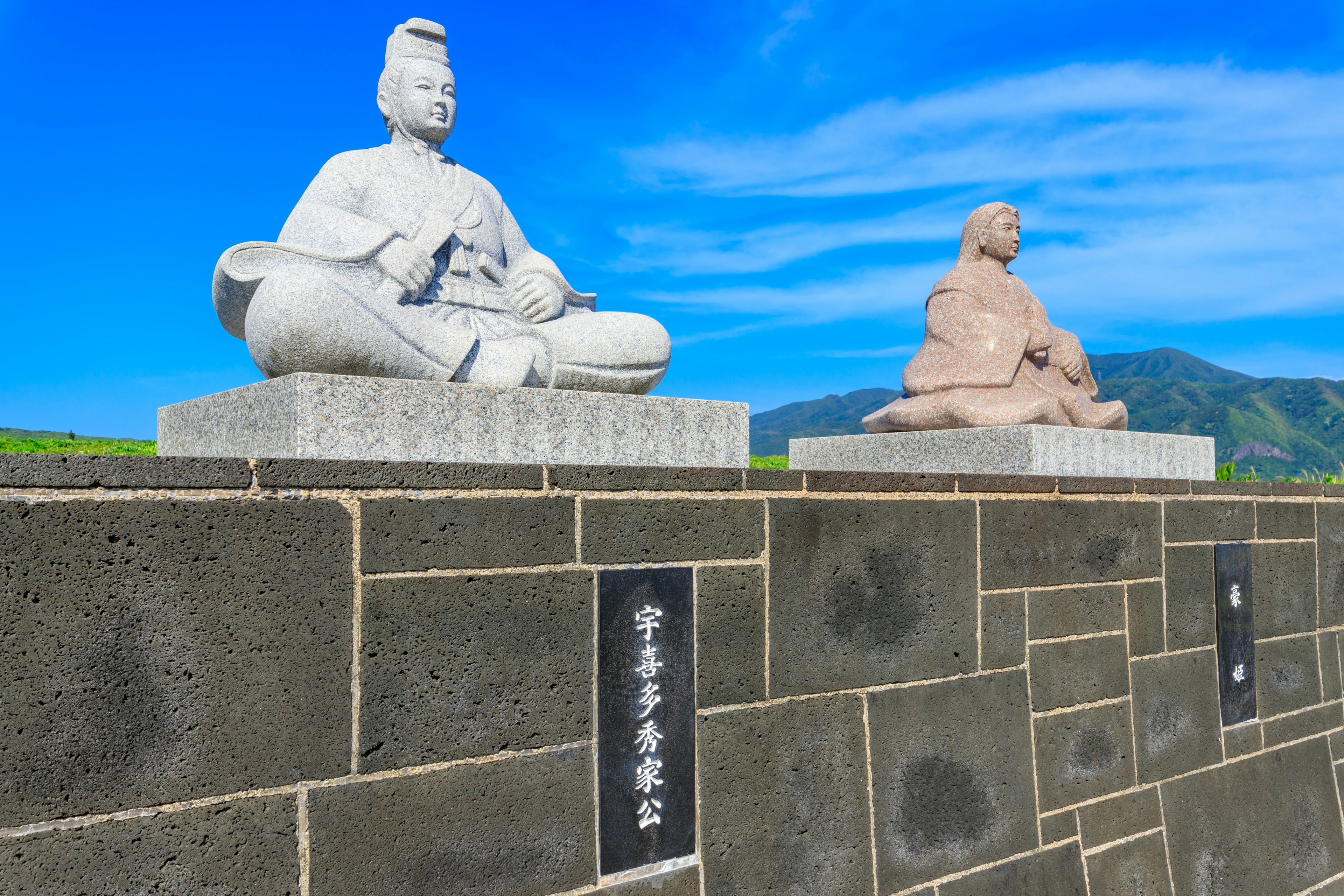 Two white statues under a blue sky one seated in a meditative pose