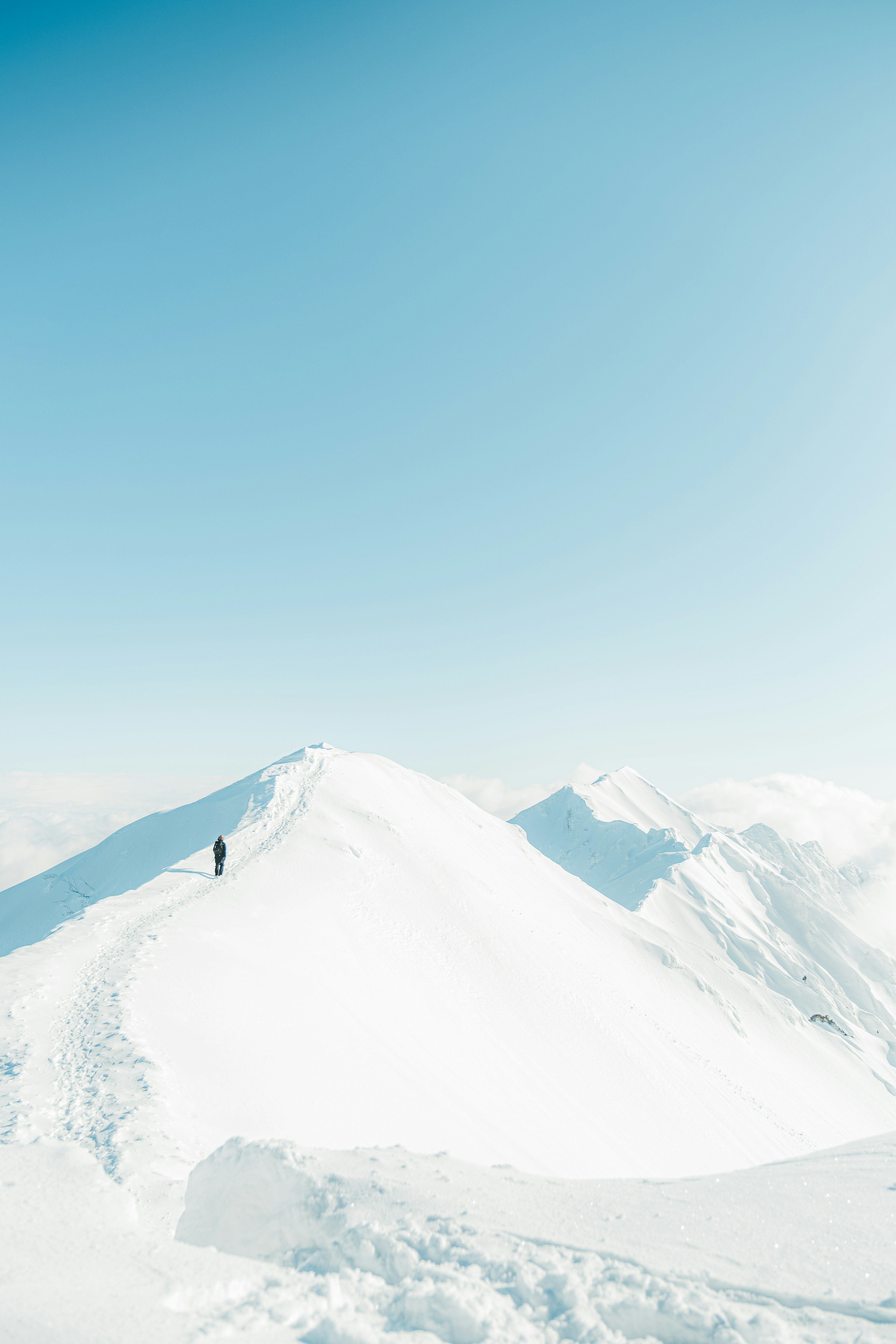 A lone hiker standing on a snow-covered mountain peak with a clear blue sky