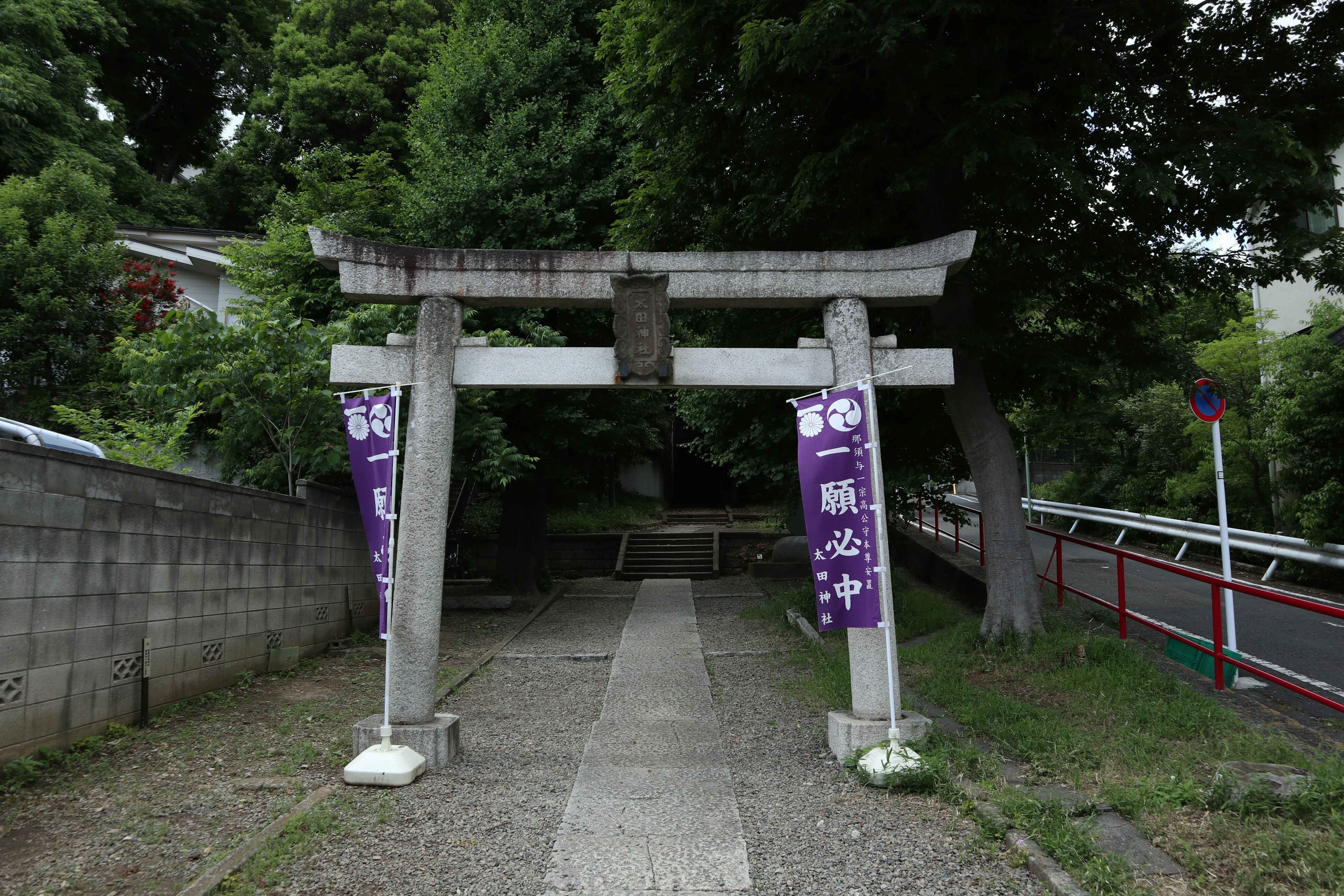 Cổng torii được bao quanh bởi cây xanh với biểu ngữ màu tím