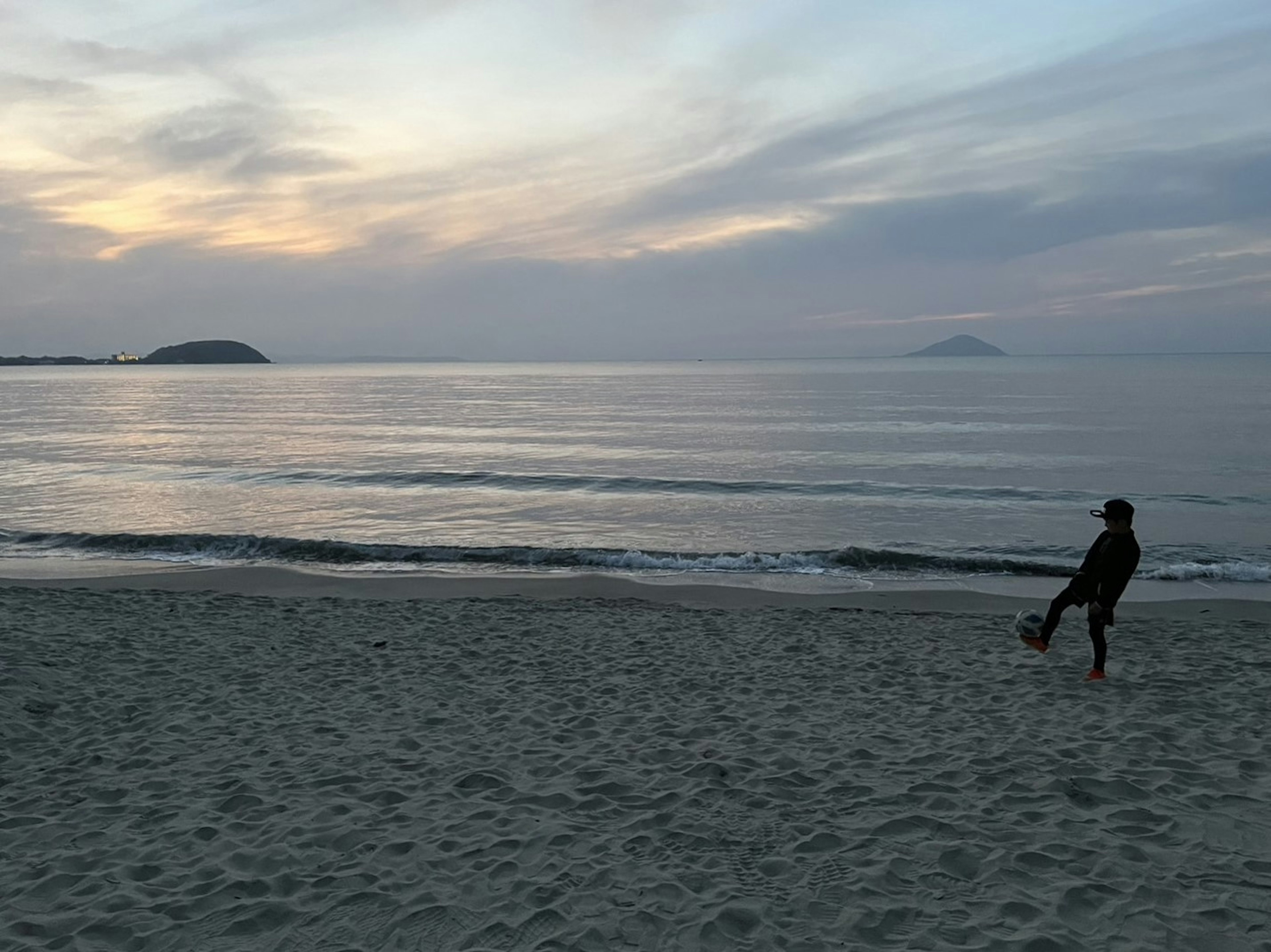 静かな海辺でサッカーボールを蹴る人のシルエットが夕焼けの空に映える