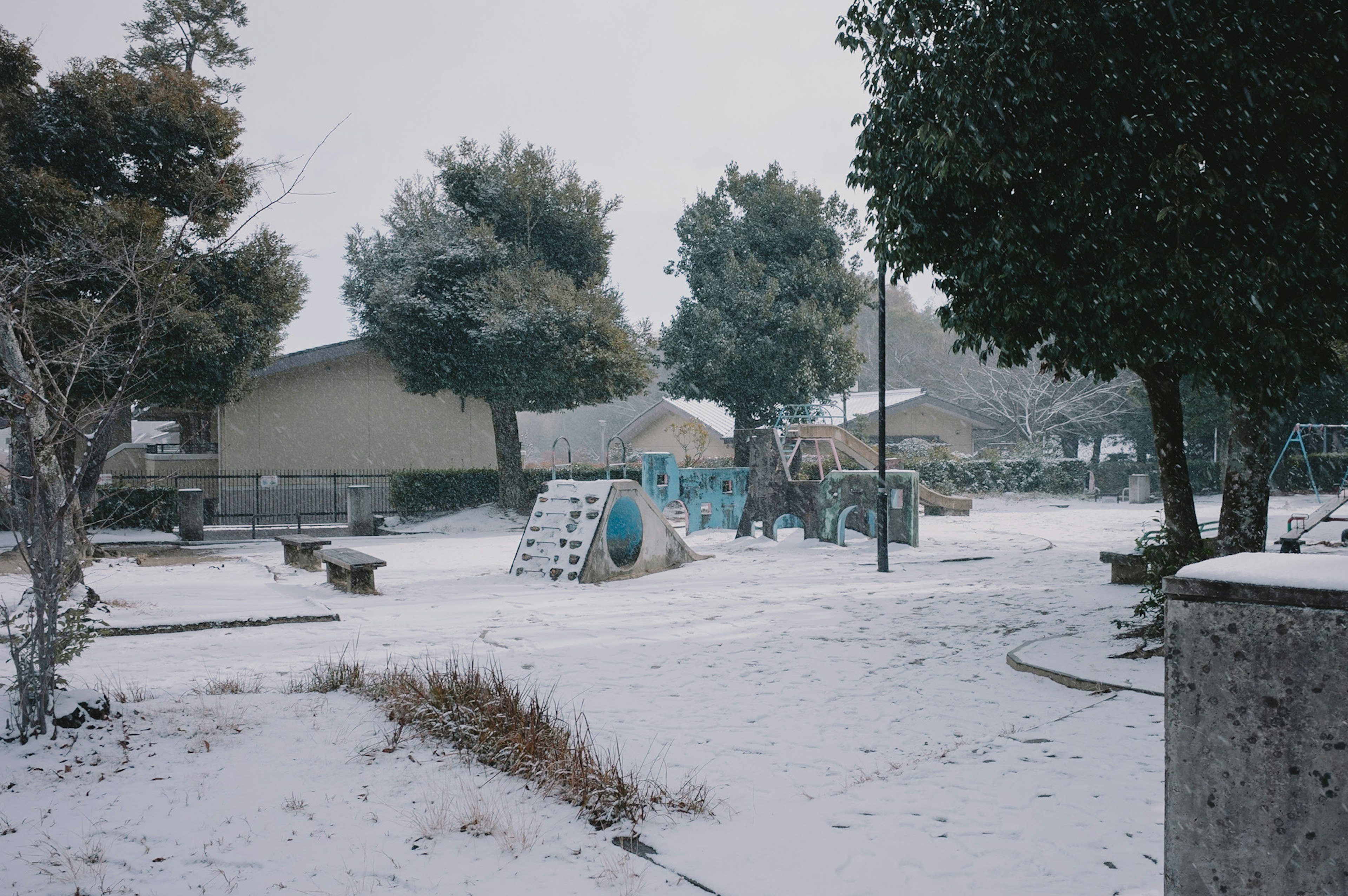 Snow-covered park scene featuring playground equipment and trees