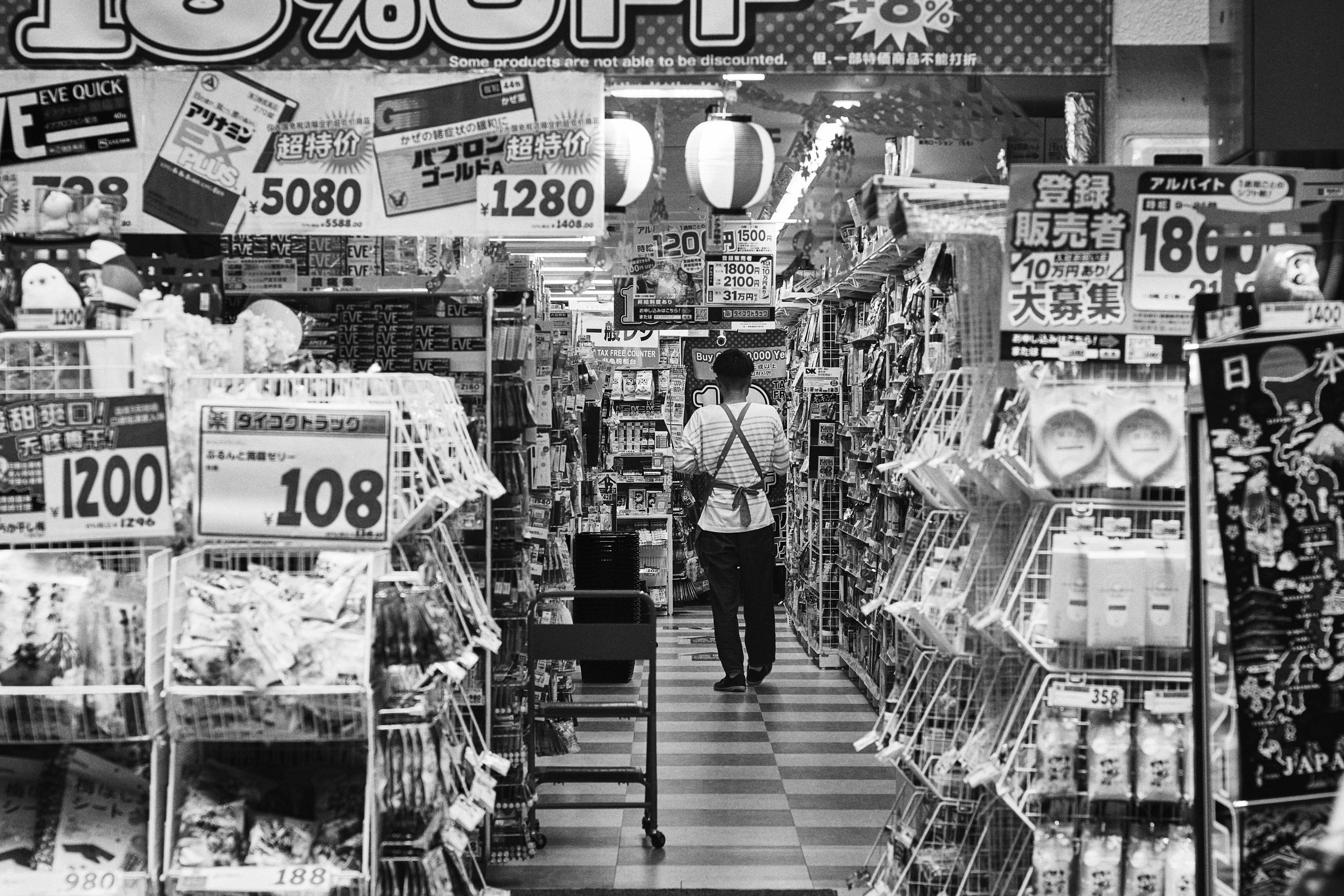 Una persona che cammina lungo un corridoio di supermercato in bianco e nero circondata da vari prodotti