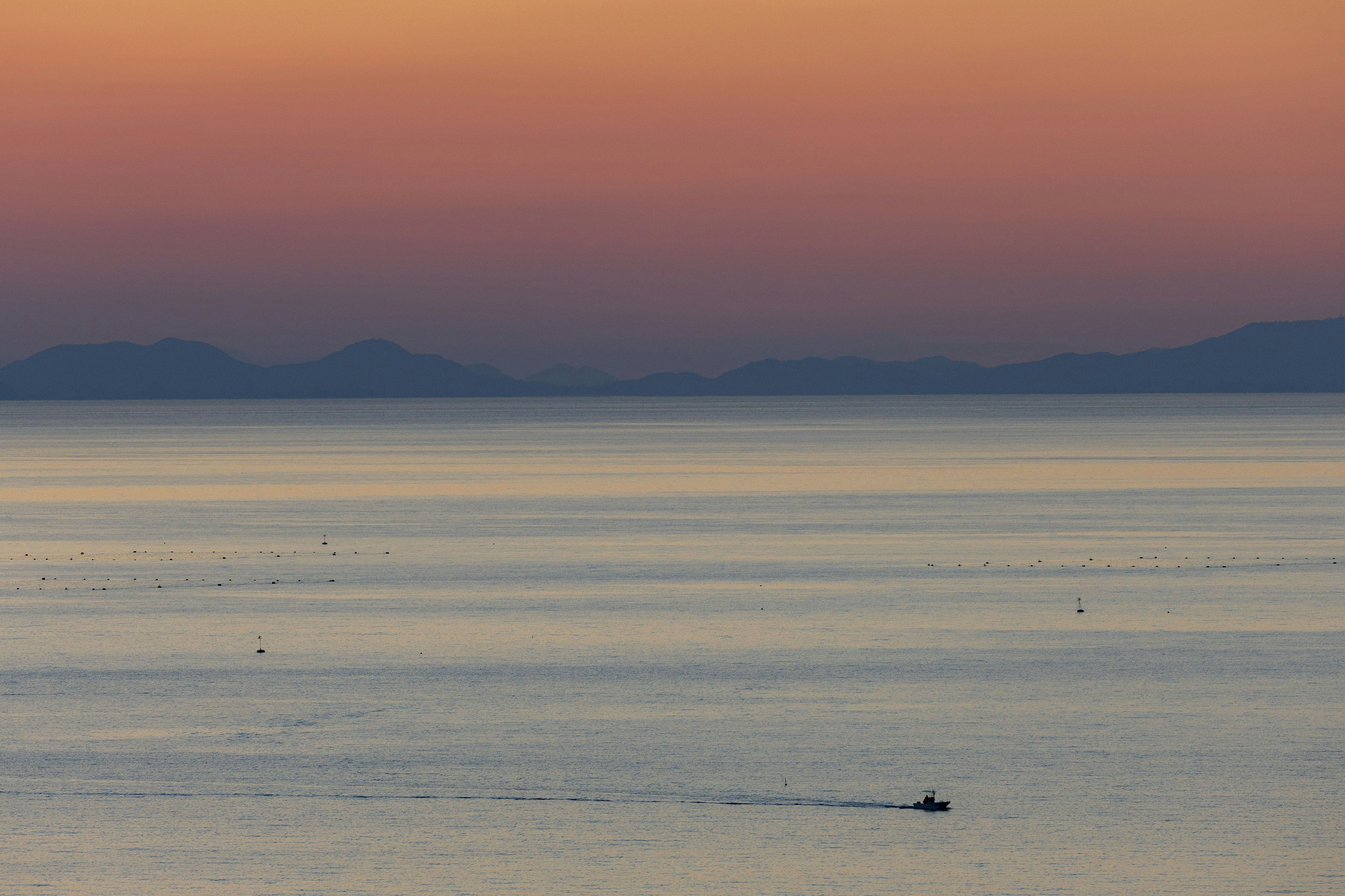 Ein kleines Boot auf einem ruhigen Meer mit einem Farbverlauf der Sonnenuntergangsfarben im Himmel und Spiegelung im Wasser