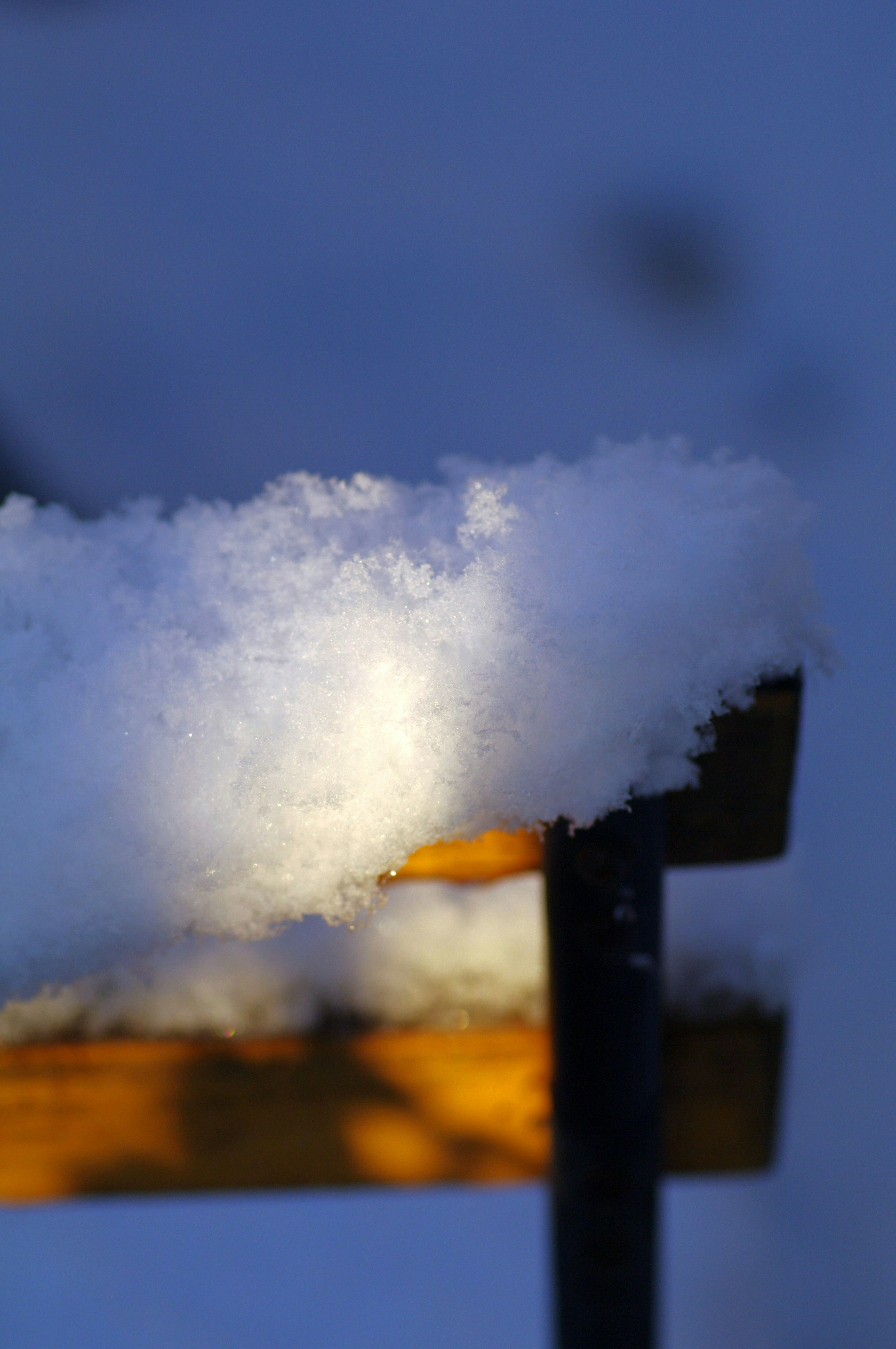 Close-up of snow on a bench with a blue background