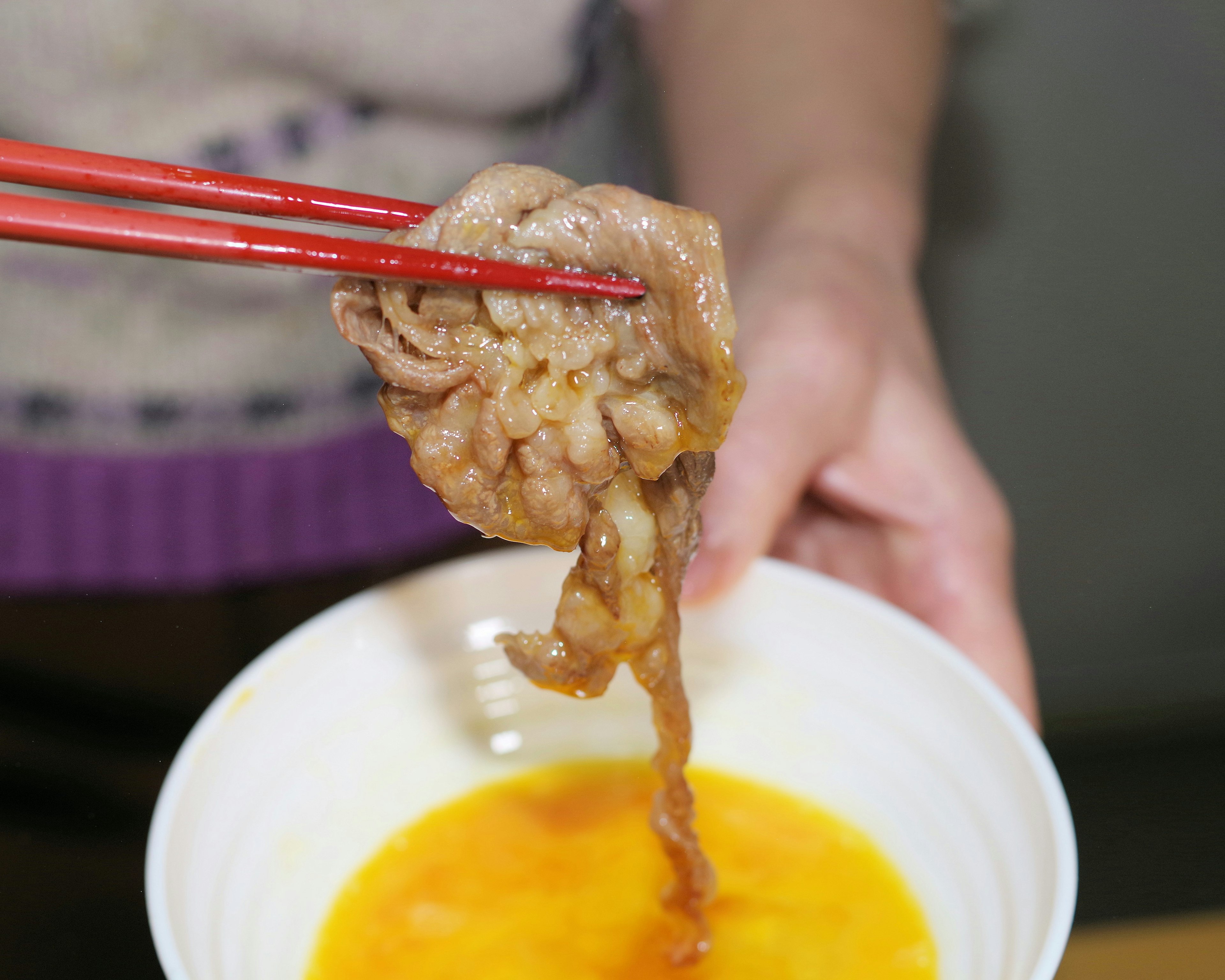 Eine Hand, die Fleisch mit roten Essstäbchen über einer Schüssel mit gelbem Ei hält