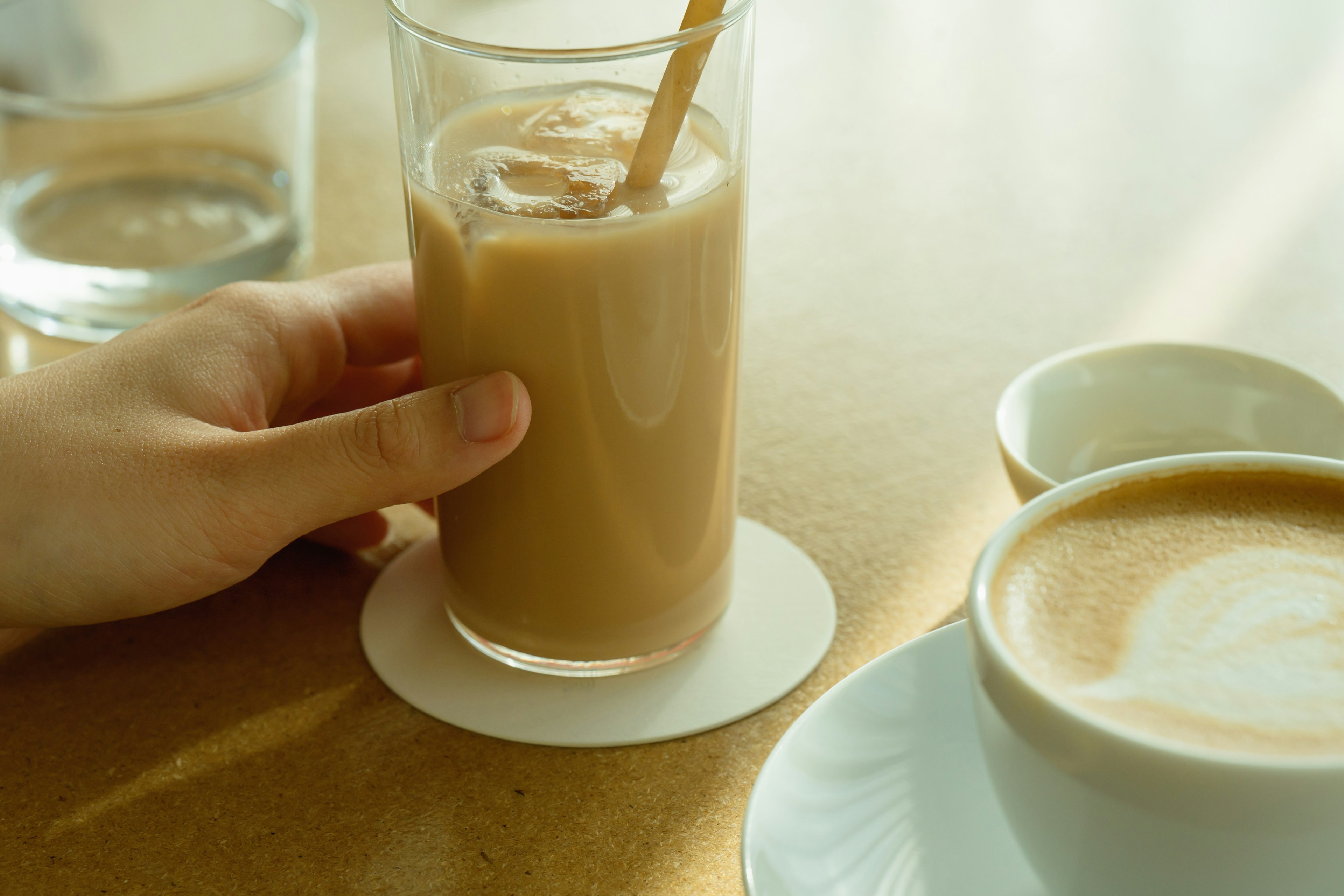 アイスコーヒーとカフェラテが並ぶテーブルの上で手がアイスコーヒーを持っている