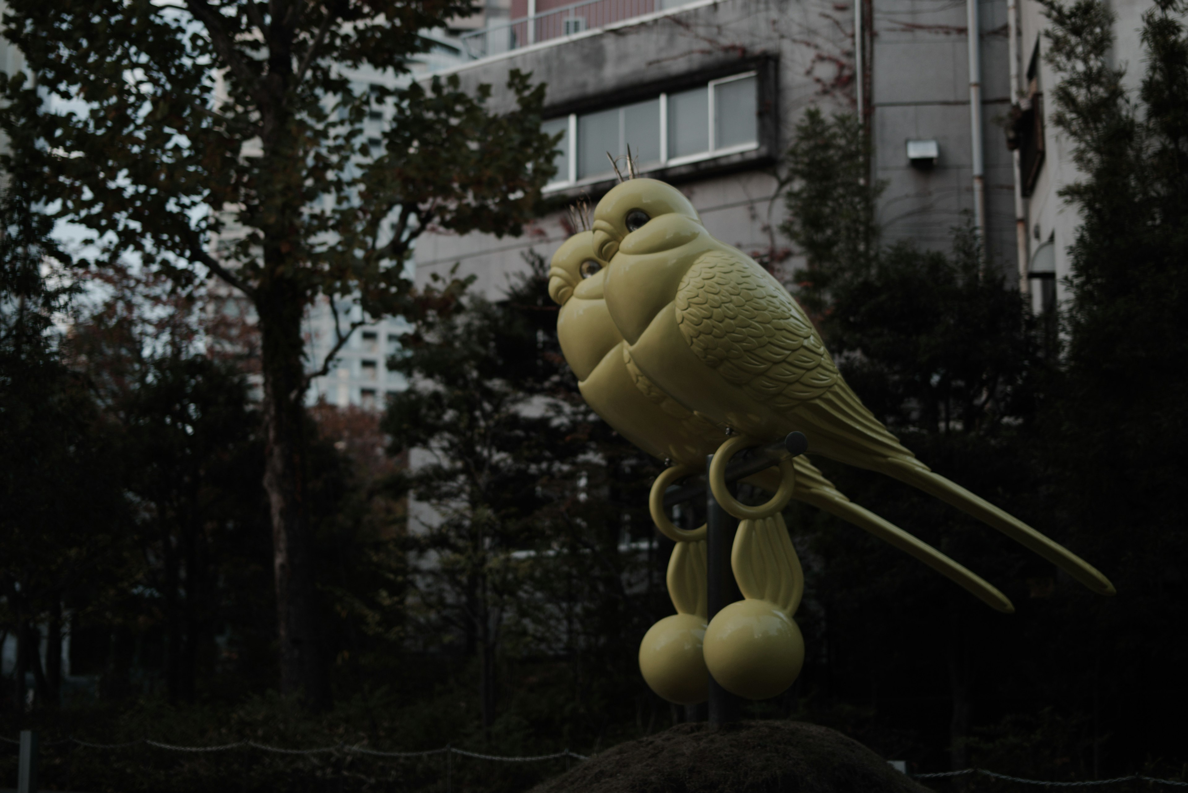 Une sculpture d'oiseau jaune se dresse contre un fond sombre dans un cadre urbain