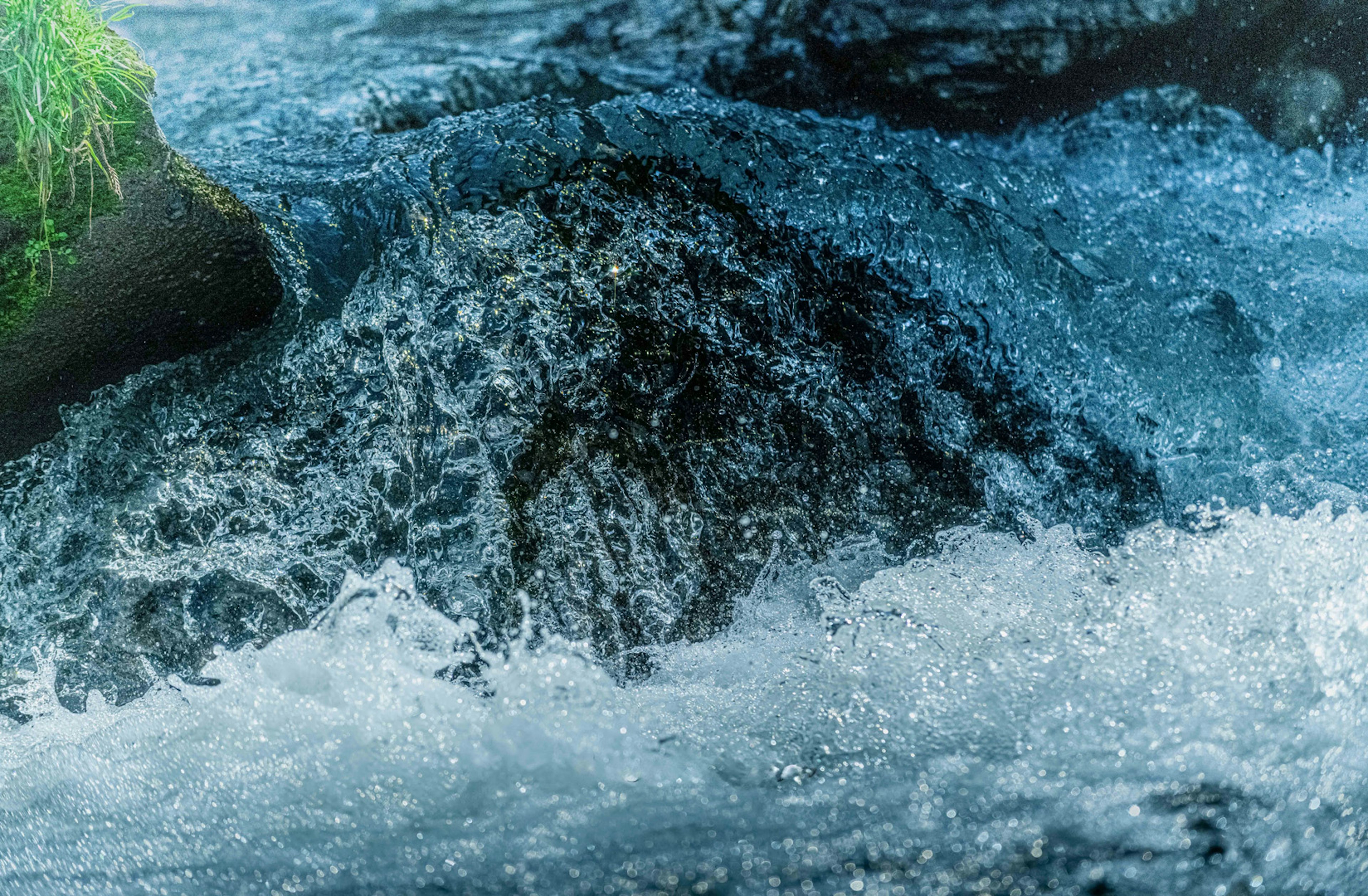 Fließendes Wasser, das über einen Felsen strömt blaues Wasser mit Spritzern und Grün