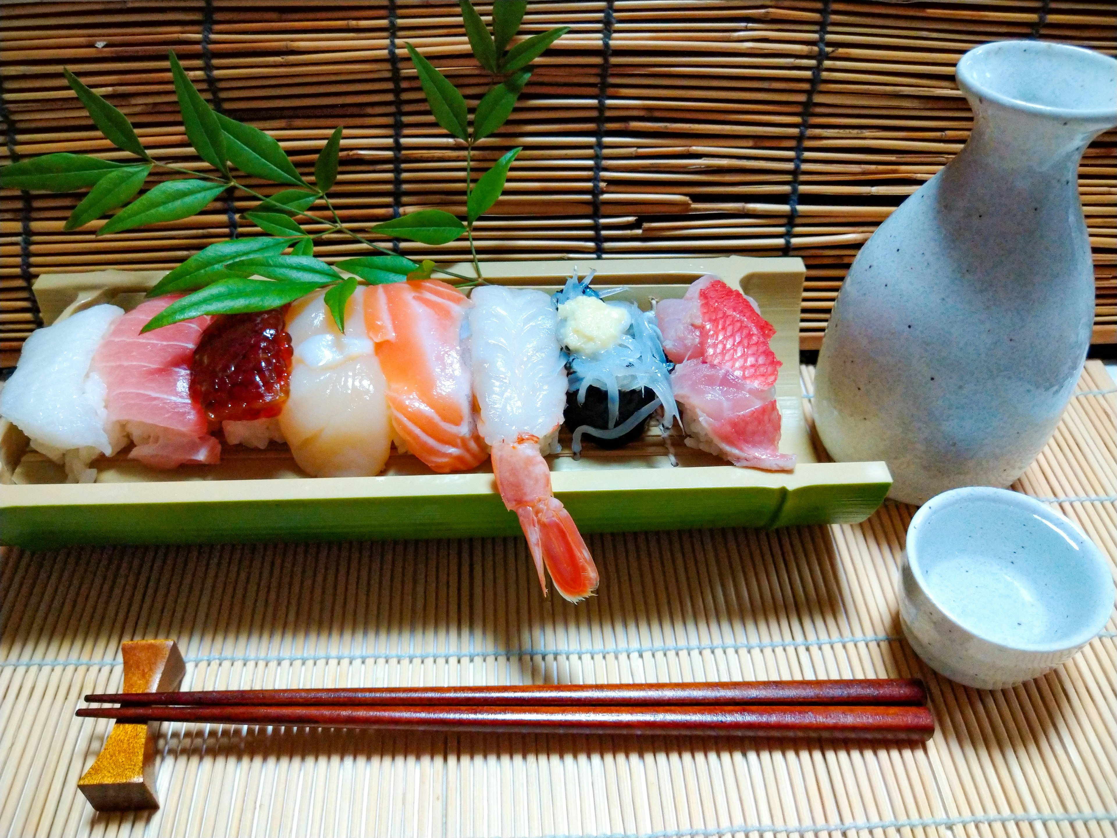 Ein Sushi-Arrangement mit verschiedenen Sushi-Sorten und einer Sake-Flasche, dekoriert mit Bambusblättern