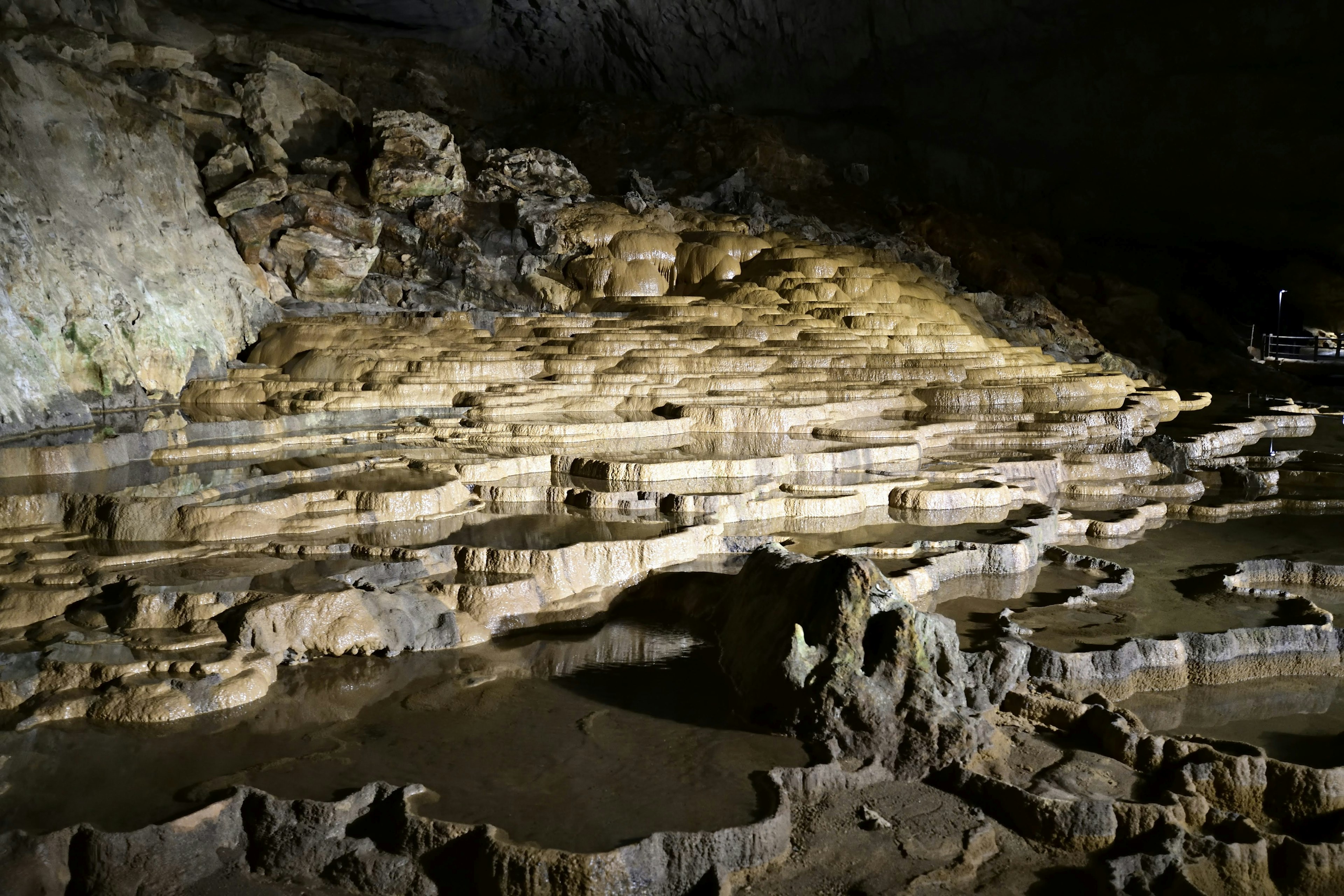 Formazioni rocciose a strati e pozzanghere in una grotta buia