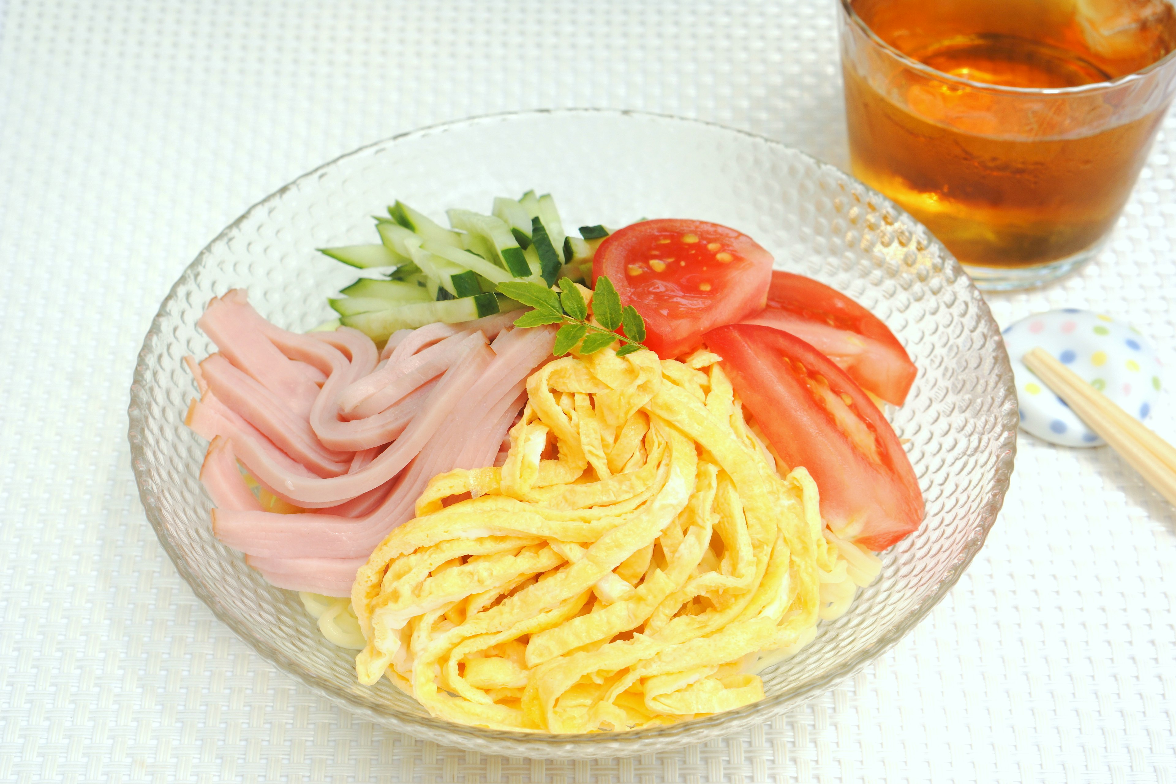 Presentación de plato de fideos fríos con jamón en rodajas, tomate, pepino y huevo