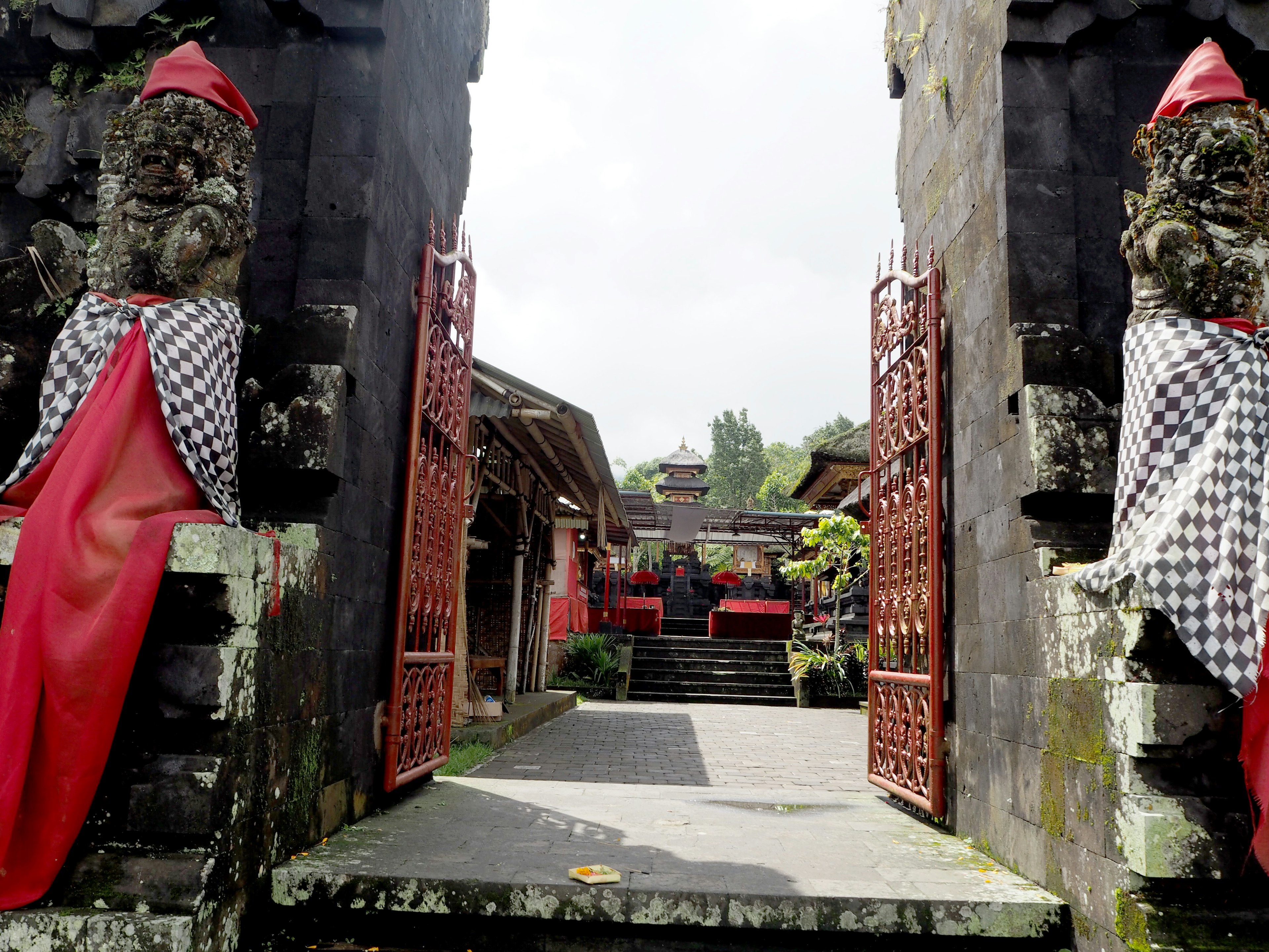 Porte d'entrée d'un temple balinais avec des statues en pierre drapées de tissu rouge