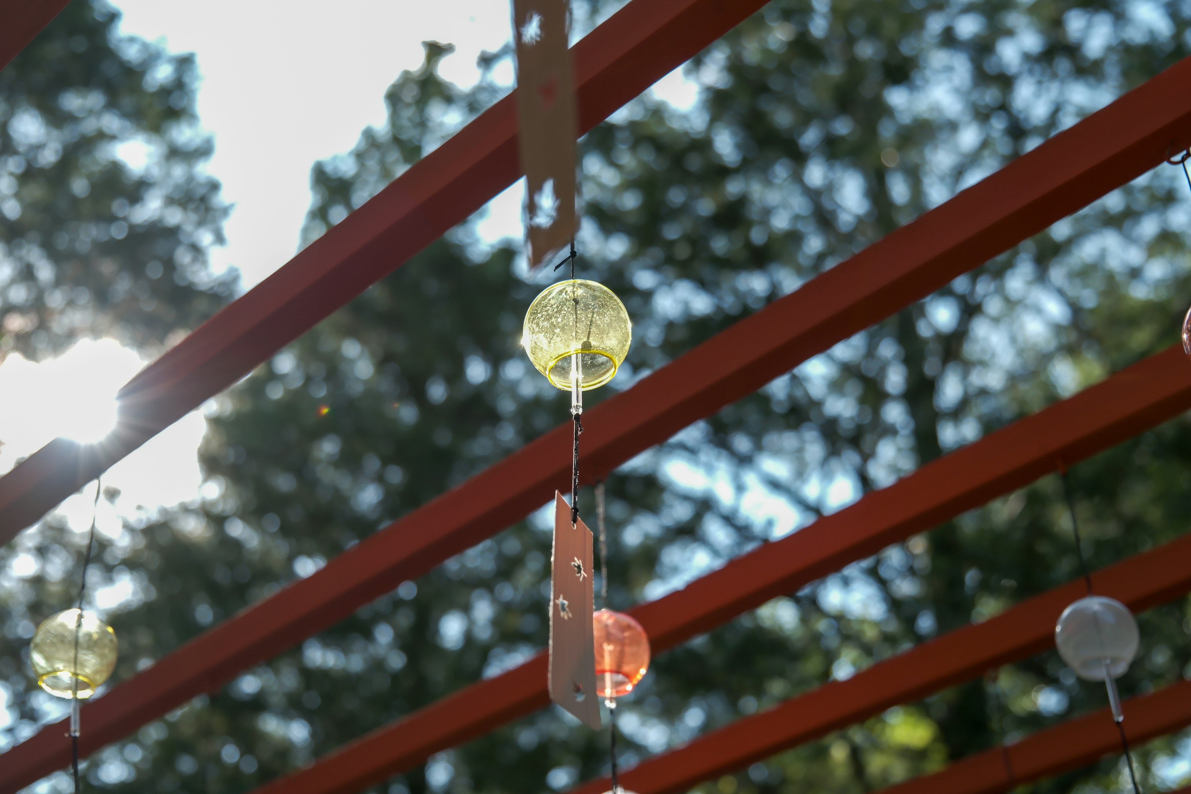 Bunte Glaskugeln hängen von roten Holzträgern mit Sonnenlicht, das durch Bäume scheint