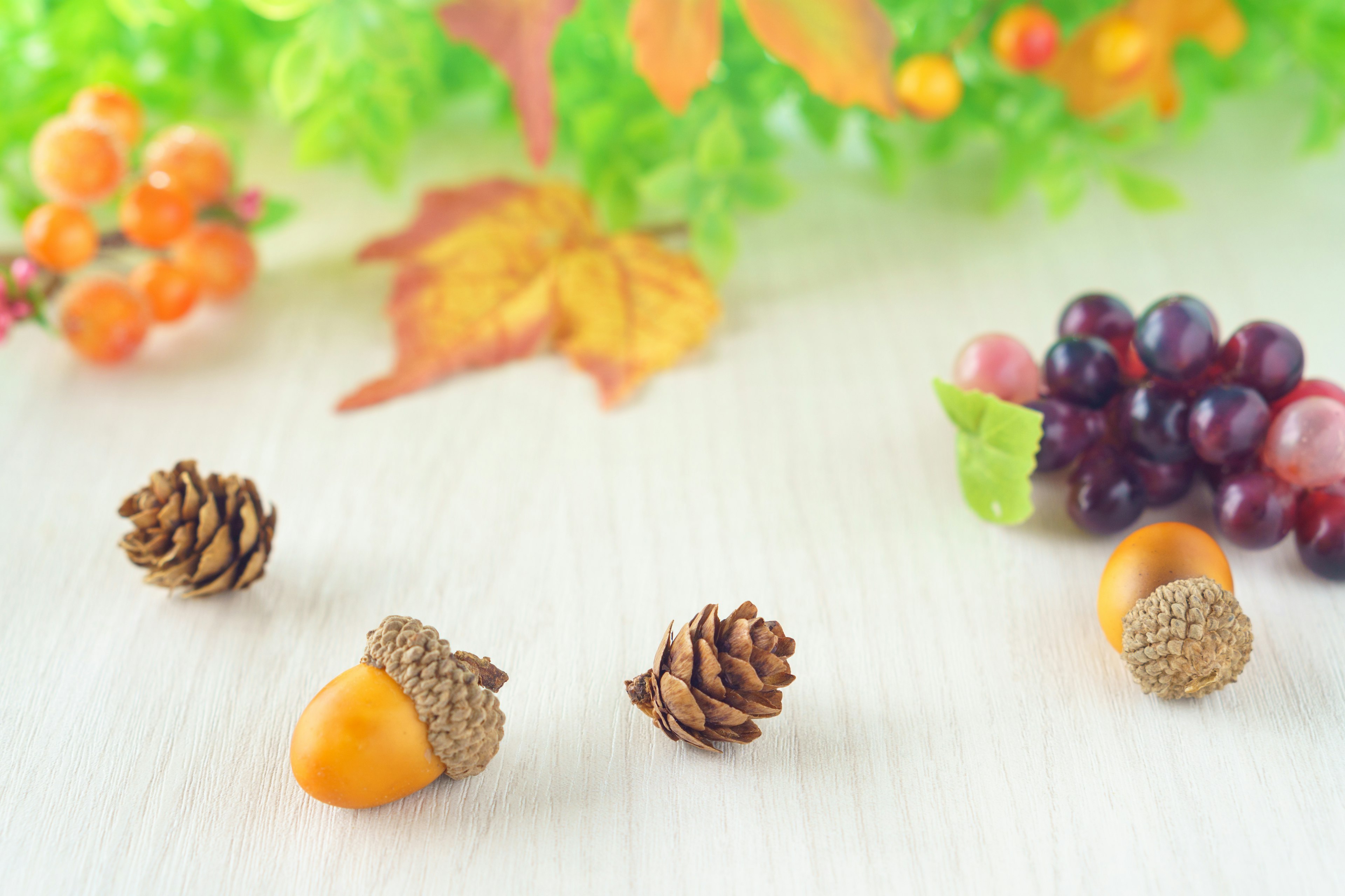 Autumn table scene featuring acorns and pine cones against a colorful backdrop of leaves and fruits