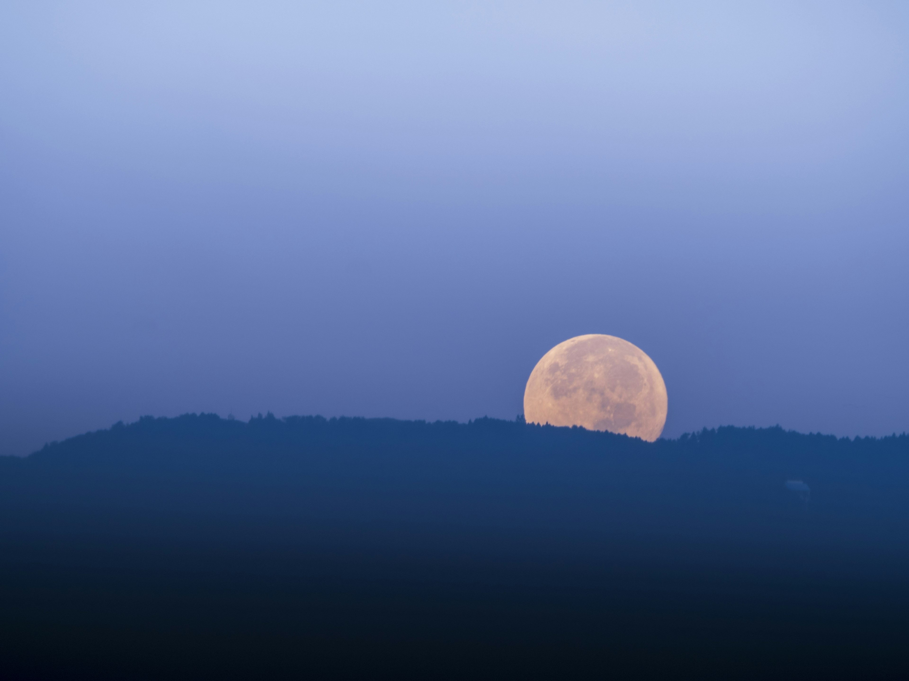 Large moon rising above the mountains under a blue sky