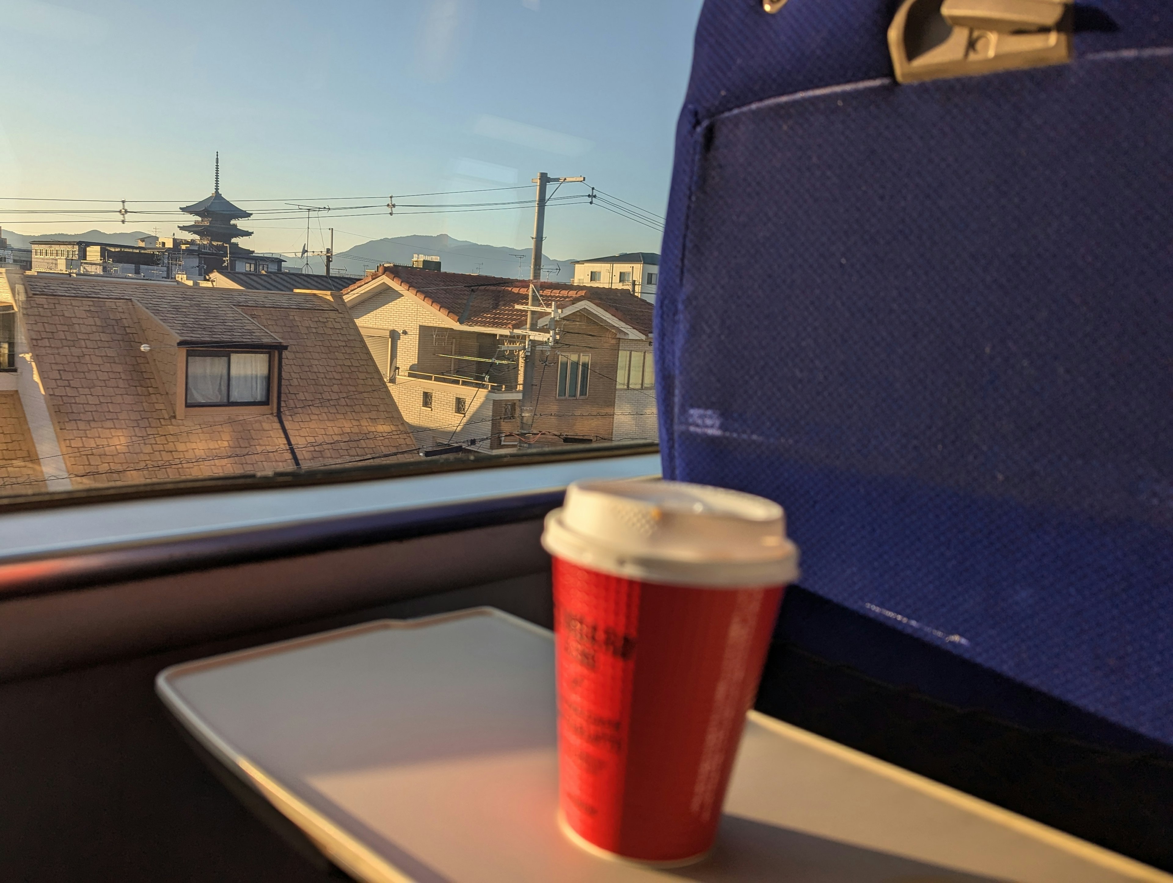 Vista desde una ventana de tren con una taza de café roja y casas