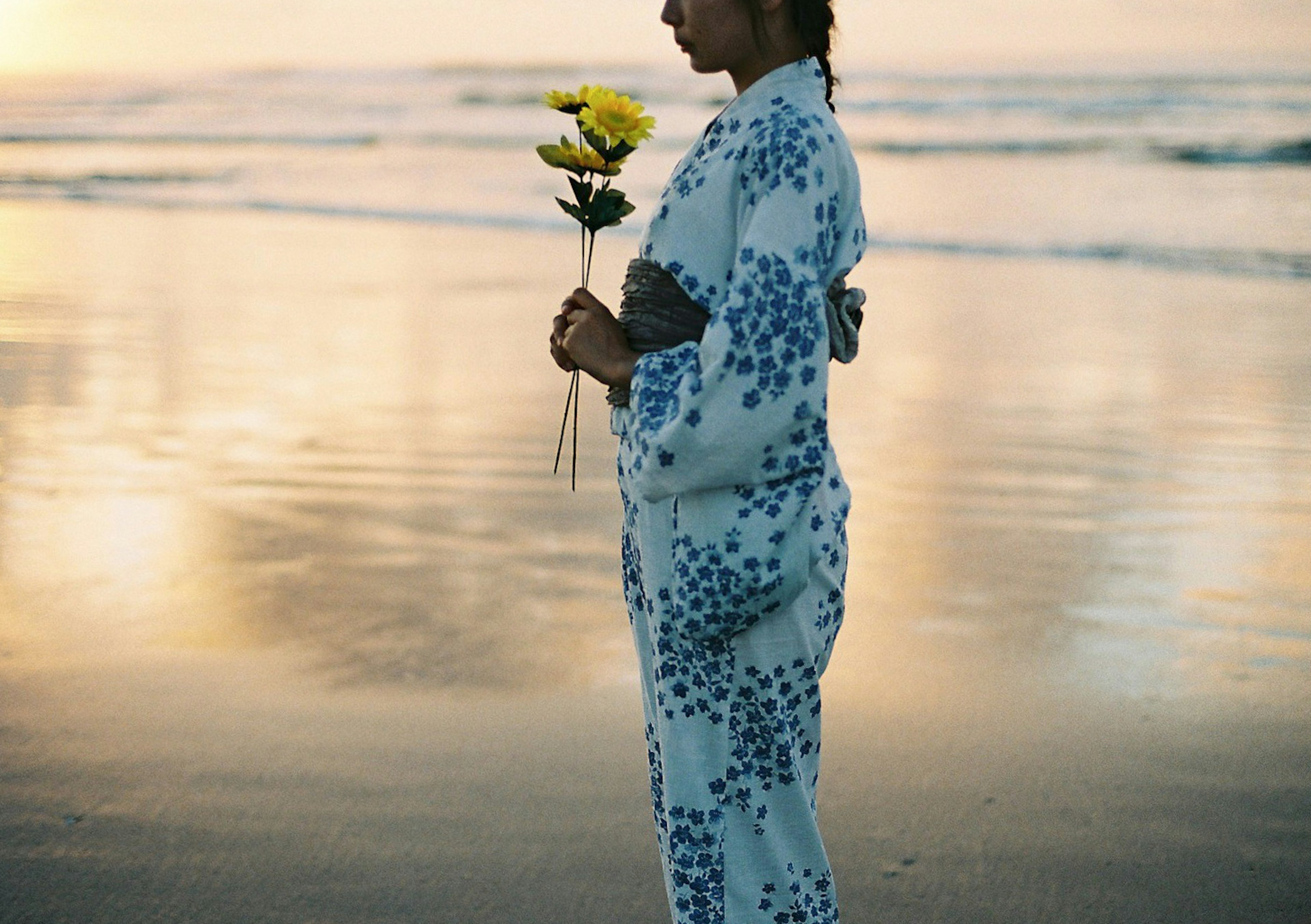 Silueta de una mujer en kimono sosteniendo flores en la playa