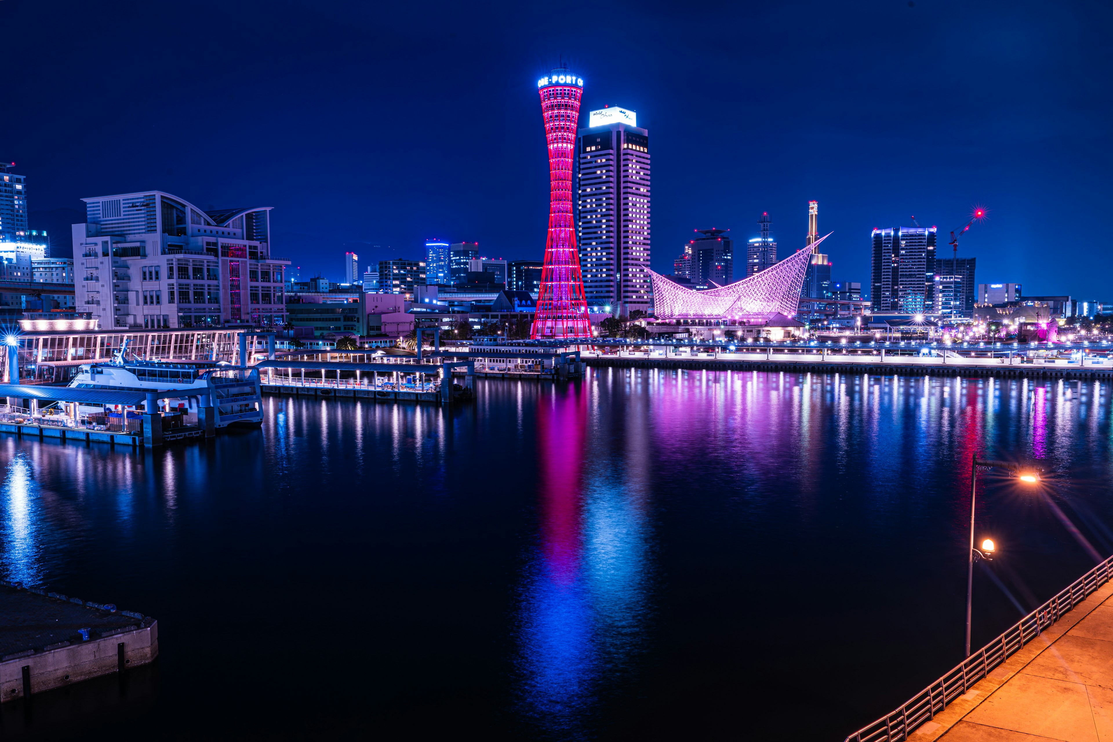 Nachtansicht von Kobe mit dem Kobe Port Tower und bunten Reflexionen auf dem Wasser