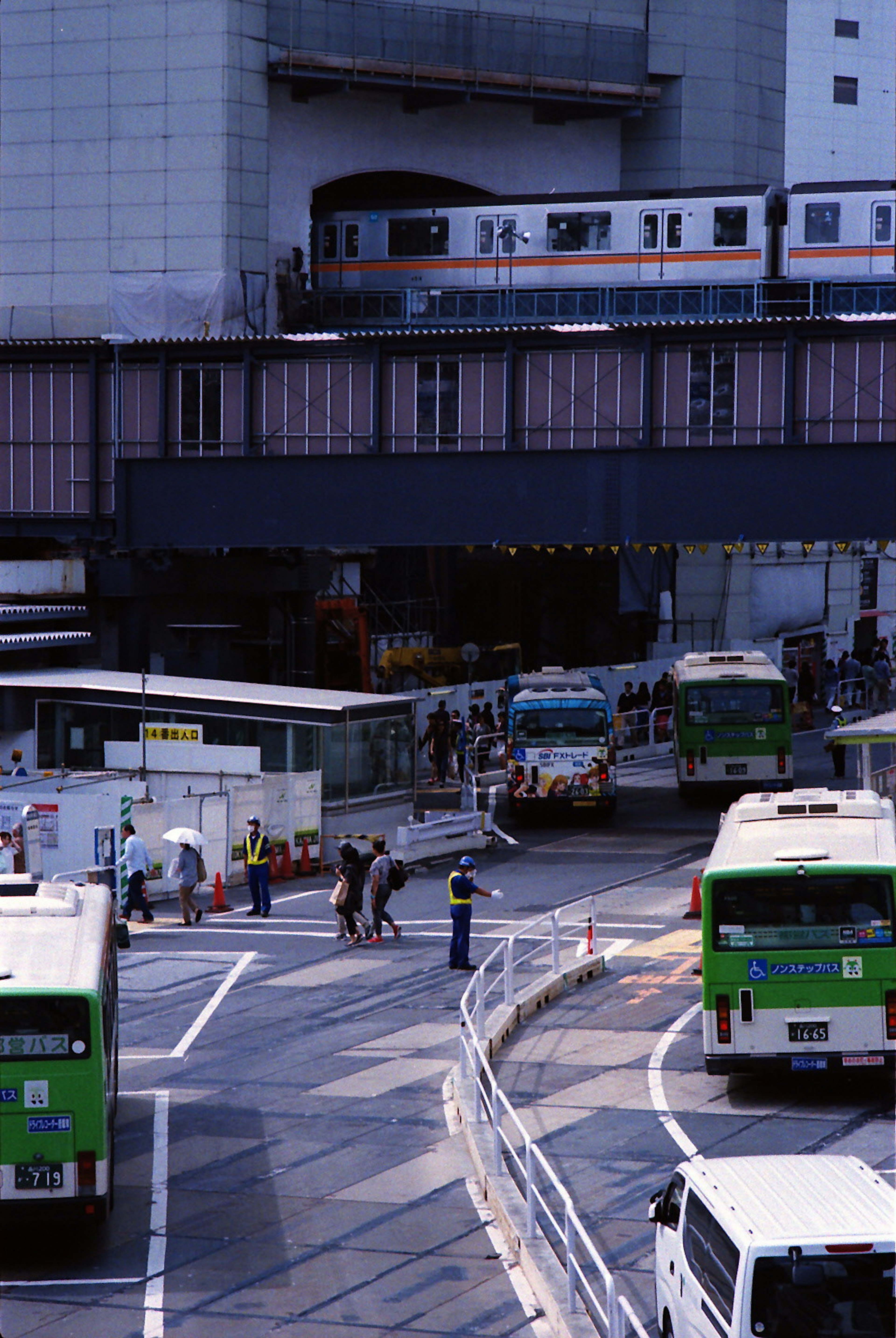 Urban intersection featuring buses and a train overhead