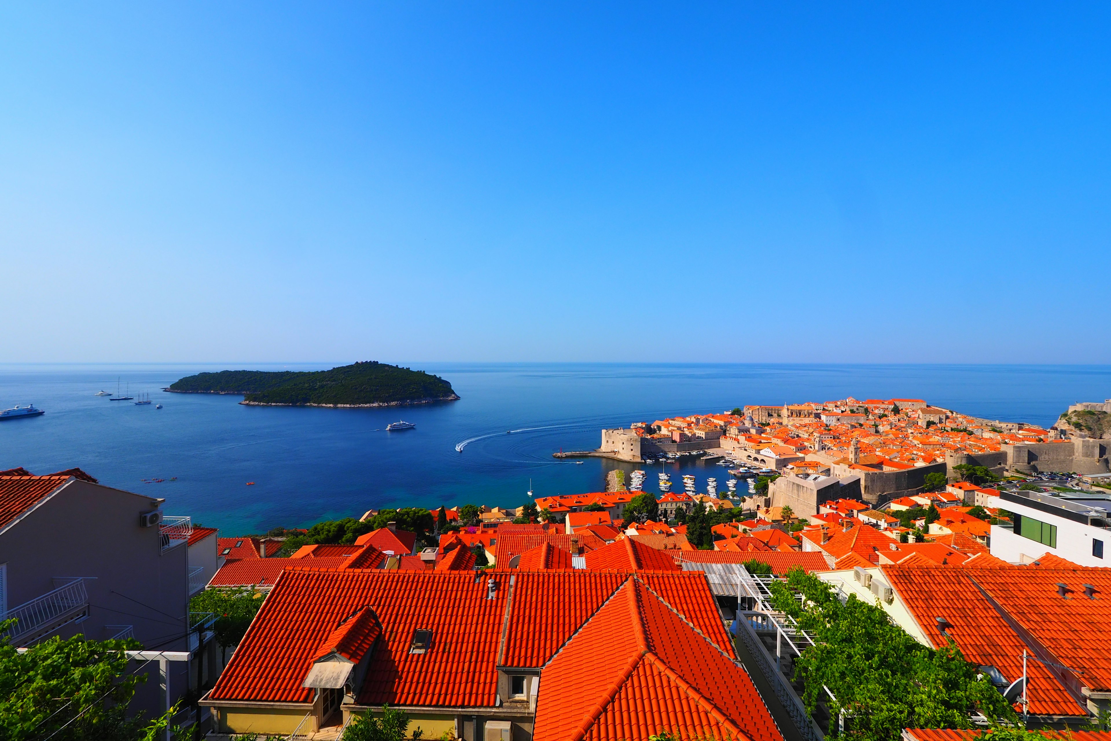 A panoramic view of Dubrovnik featuring red-roofed houses against a blue sky and sea